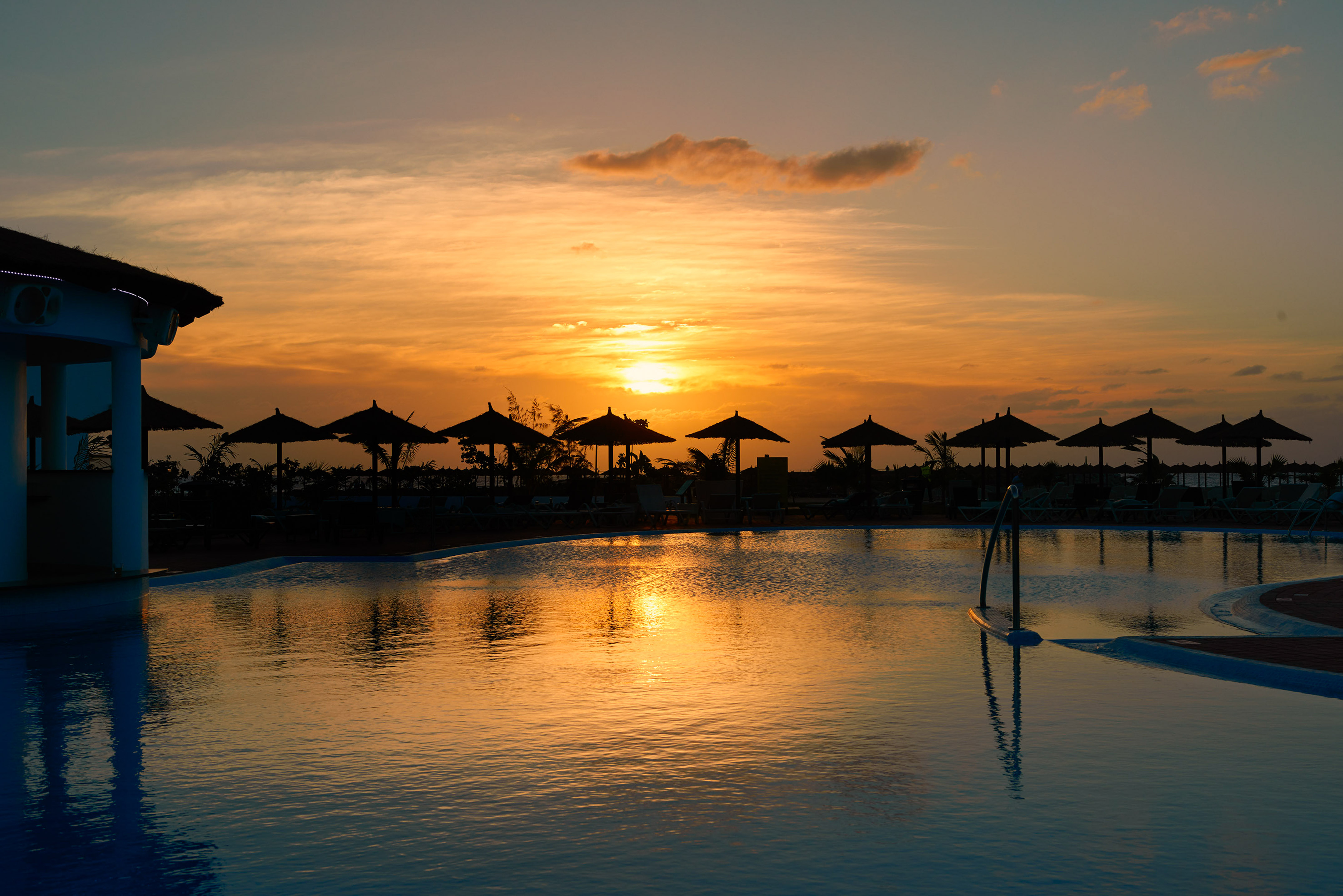 a pool with umbrellas and a sunset