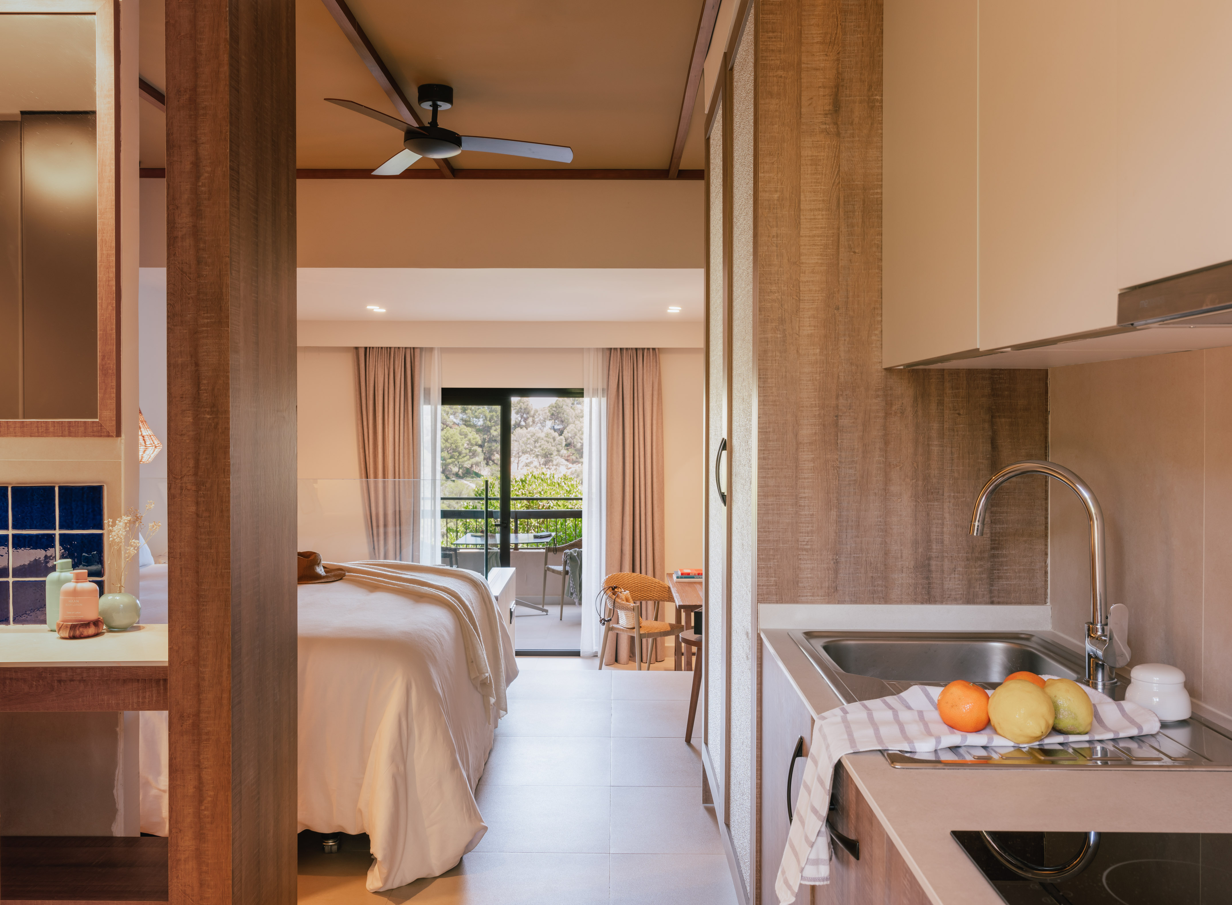 Modern studio with bedroom, balcony view, and kitchenette with fresh fruit.