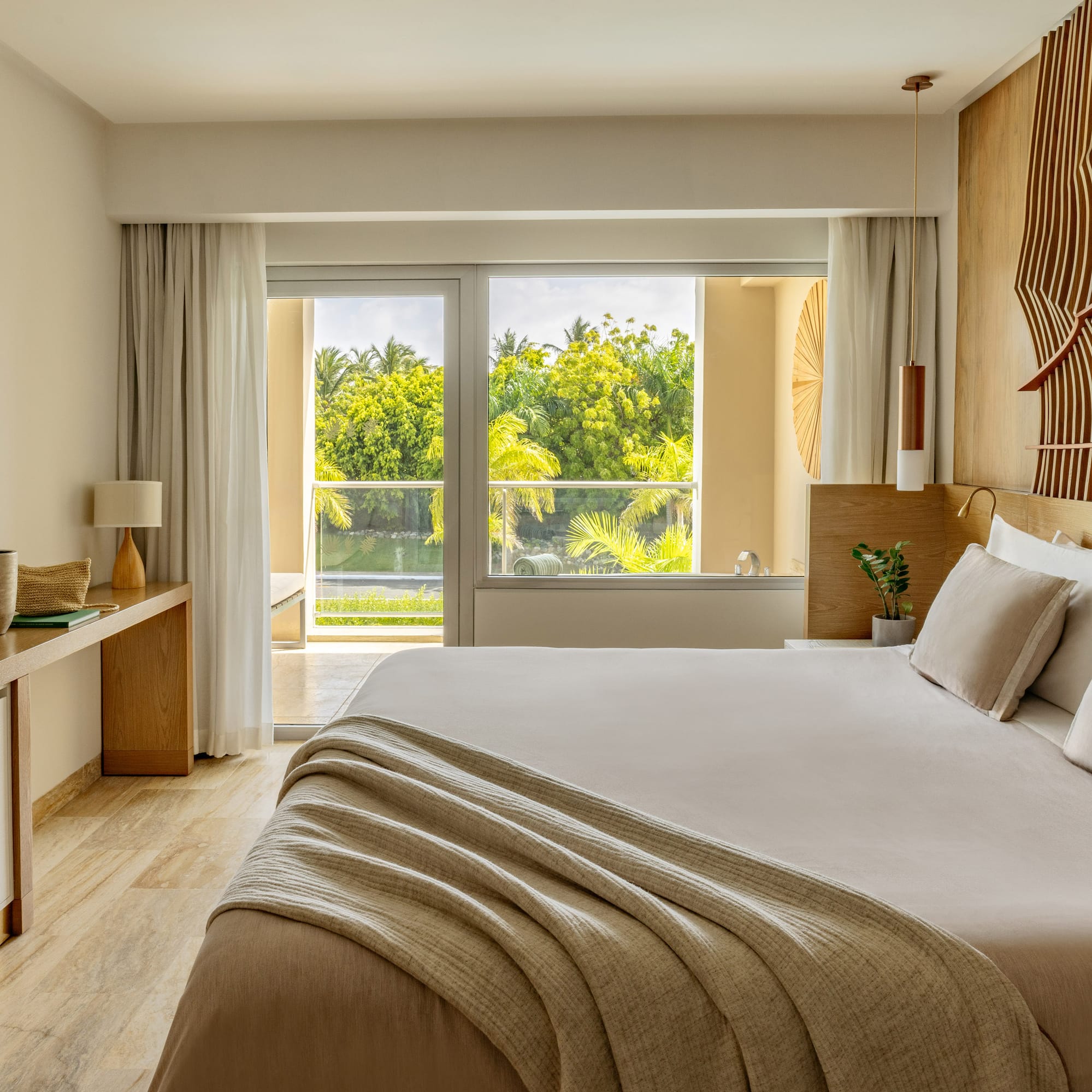 Modern hotel bedroom with king bed, lush tropical view, and decorative wood wall.