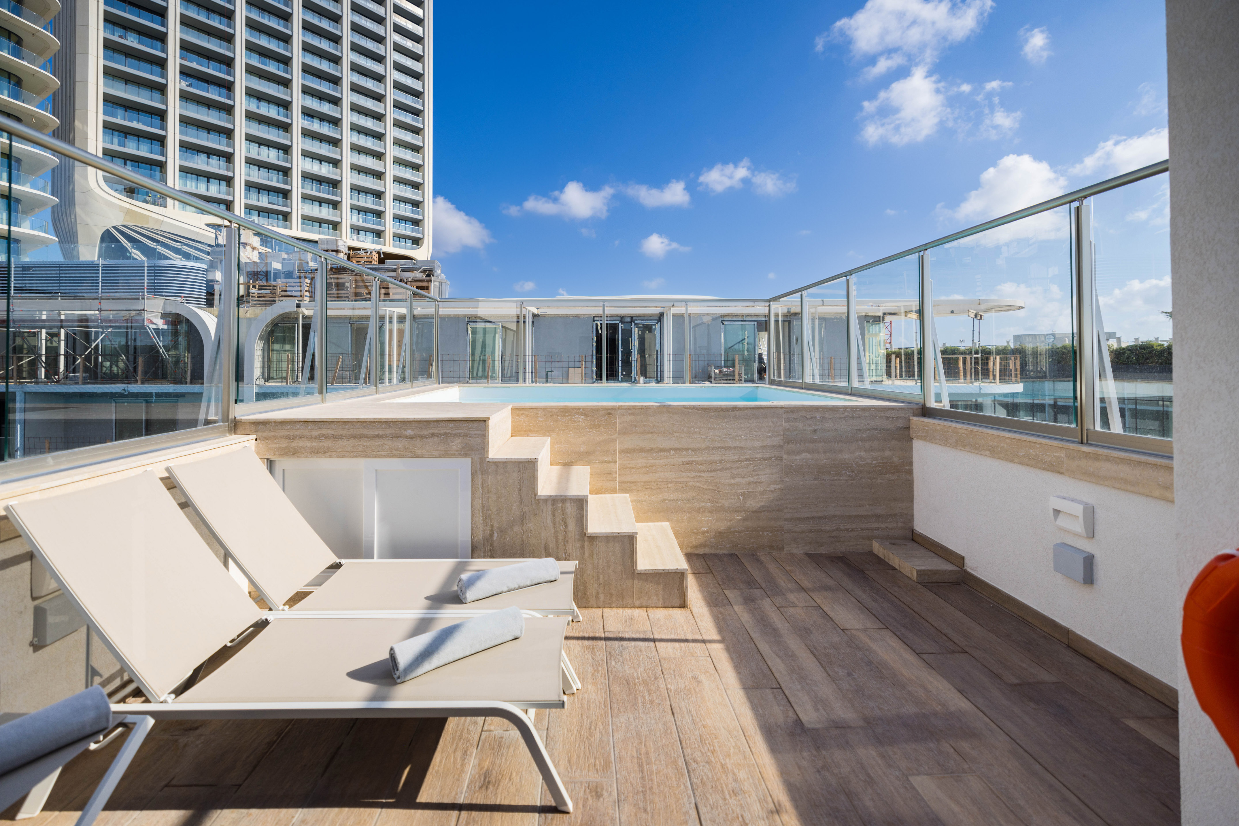 Modern hotel terrace with private pool, lounge chairs, and city high-rise view.