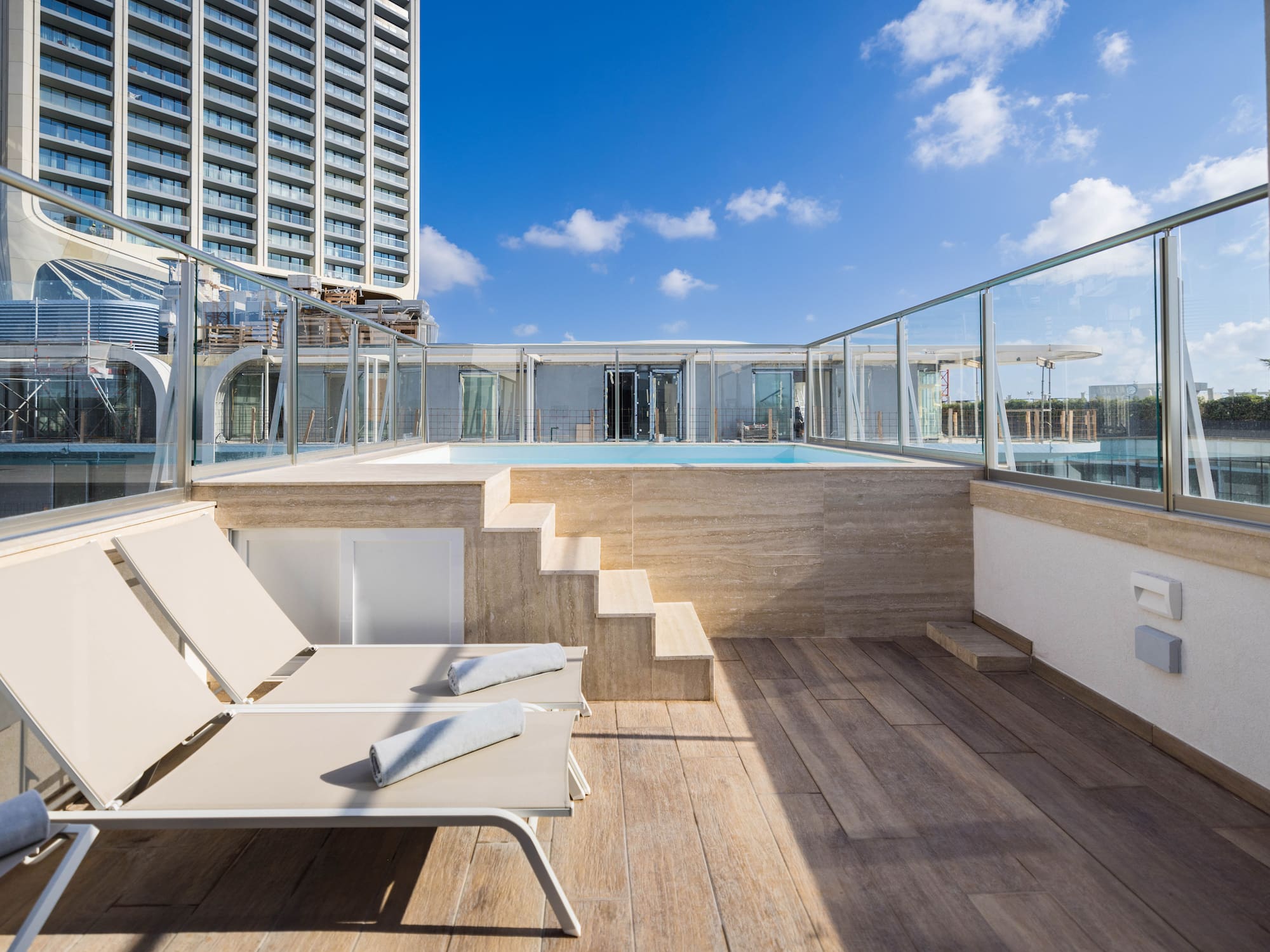 Modern hotel terrace with private pool, lounge chairs, and city high-rise view.