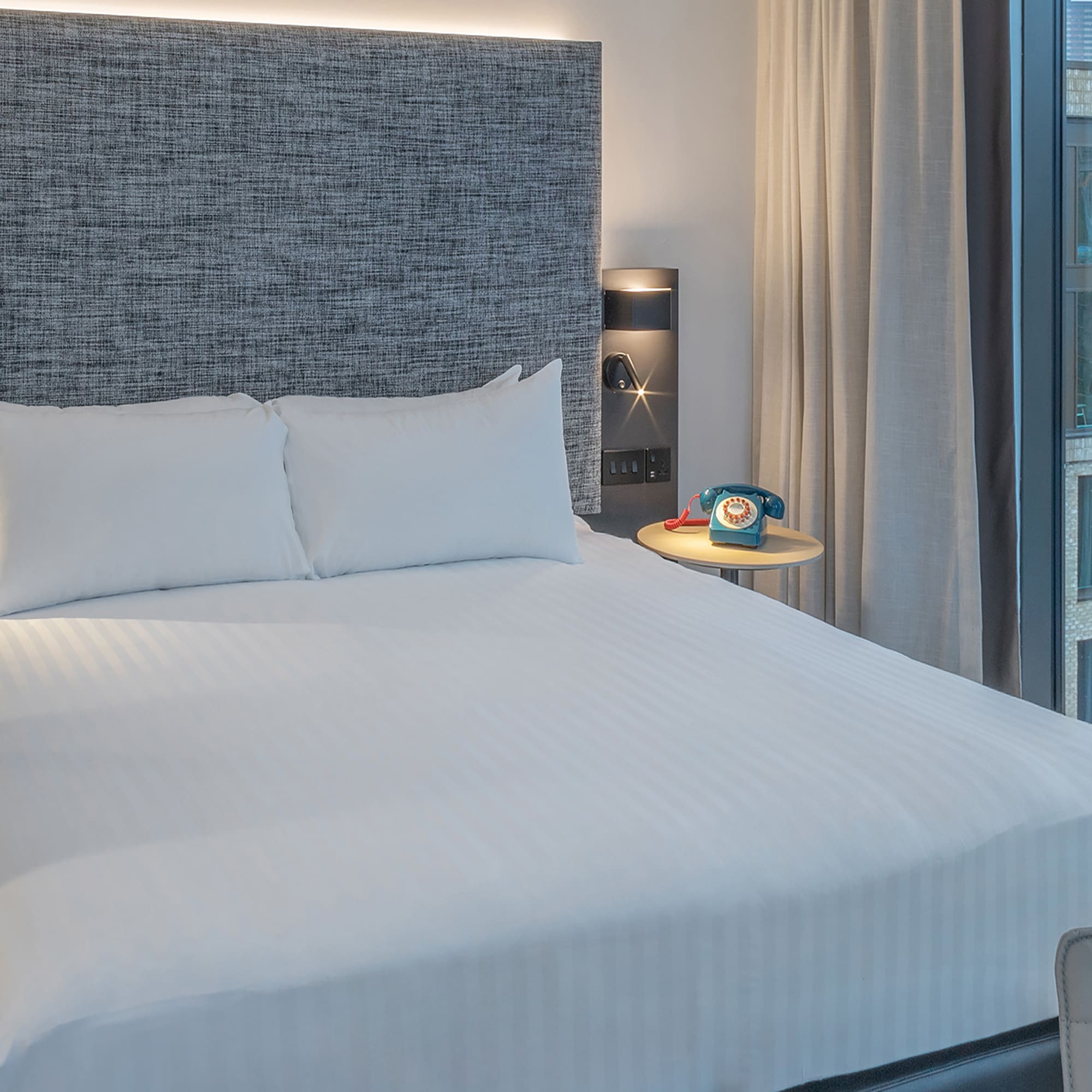 a bed with a headboard and a table with a telephone on it