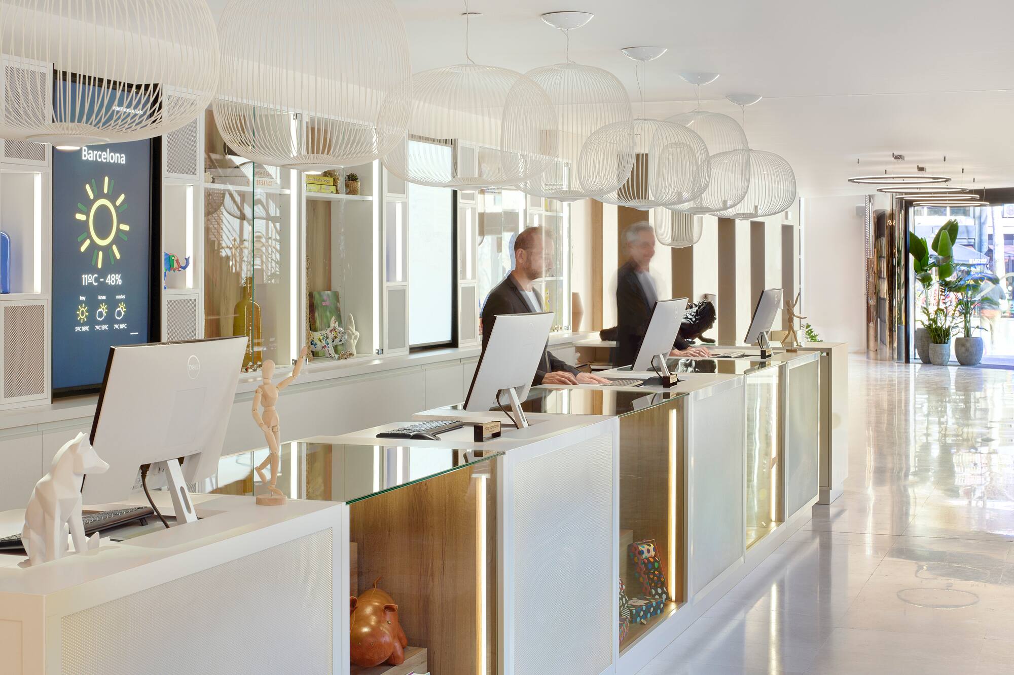 Modern hotel reception in Barcelona with staff and digital weather screen.
