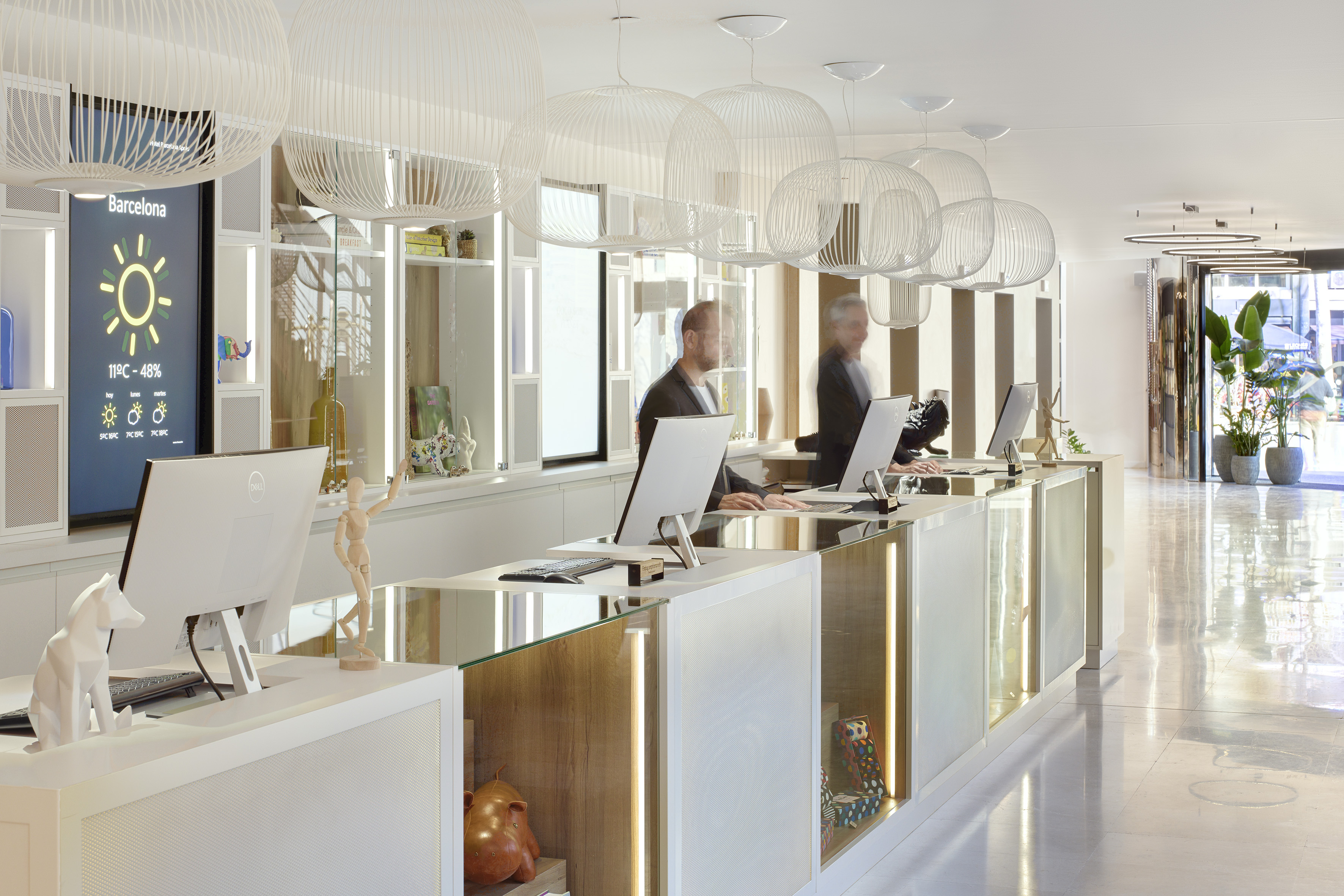 Modern hotel reception in Barcelona with staff and digital weather screen.