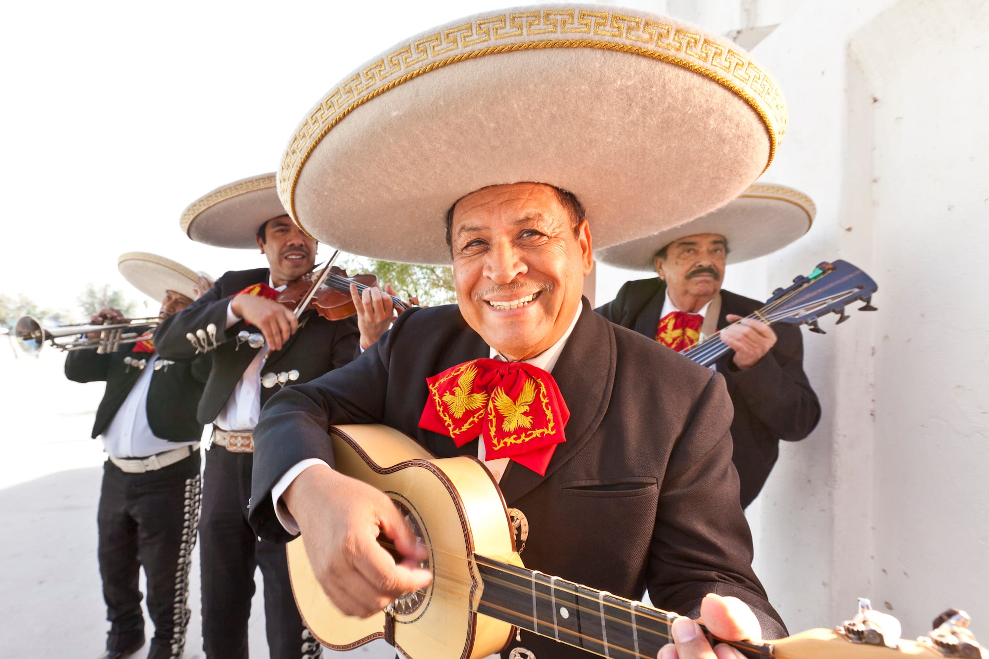 Mariachis mexicanos sonrientes con sombreros y trajes, tocando guitarra y violín.