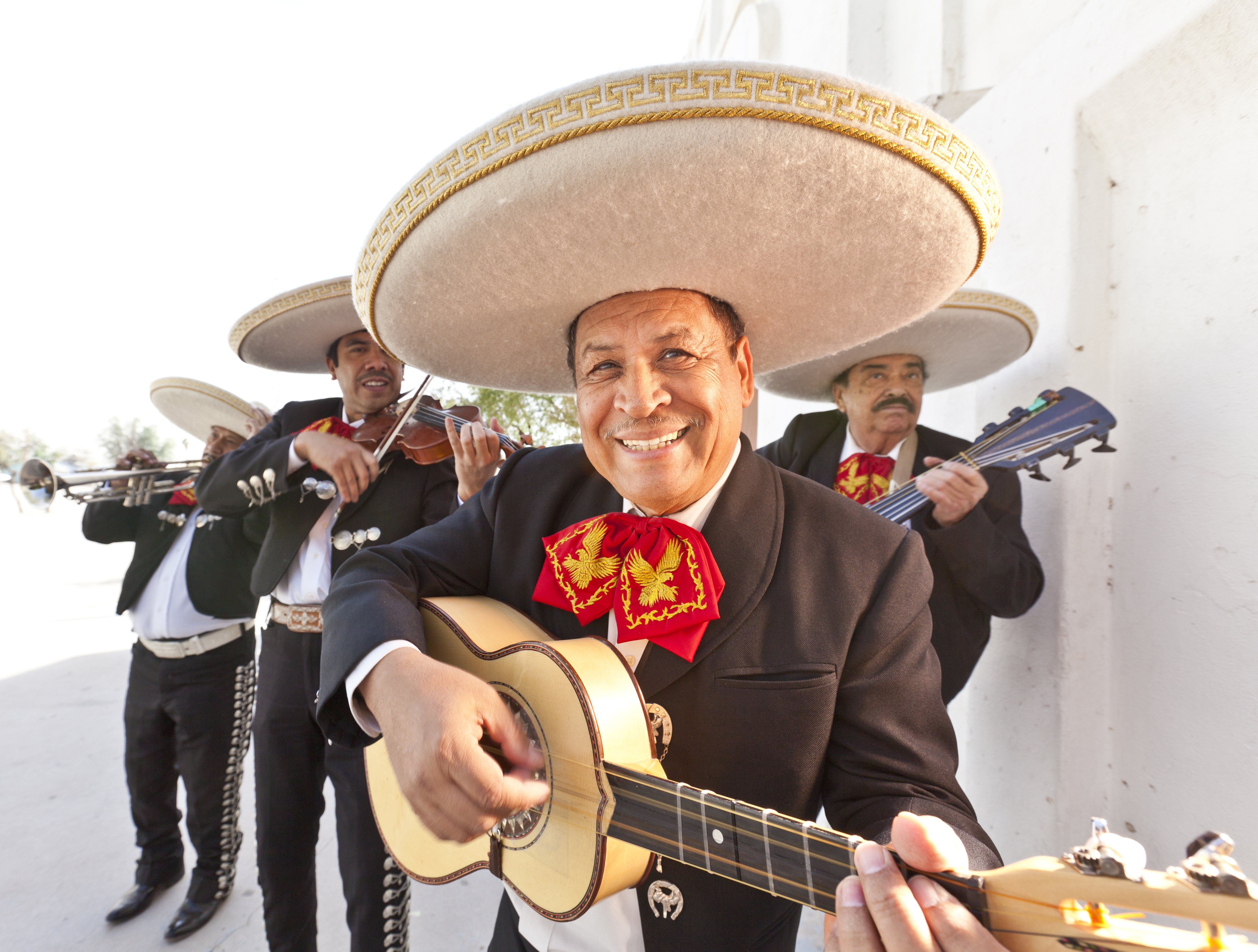 Mariachis mexicanos sonrientes con sombreros y trajes, tocando guitarra y violín.