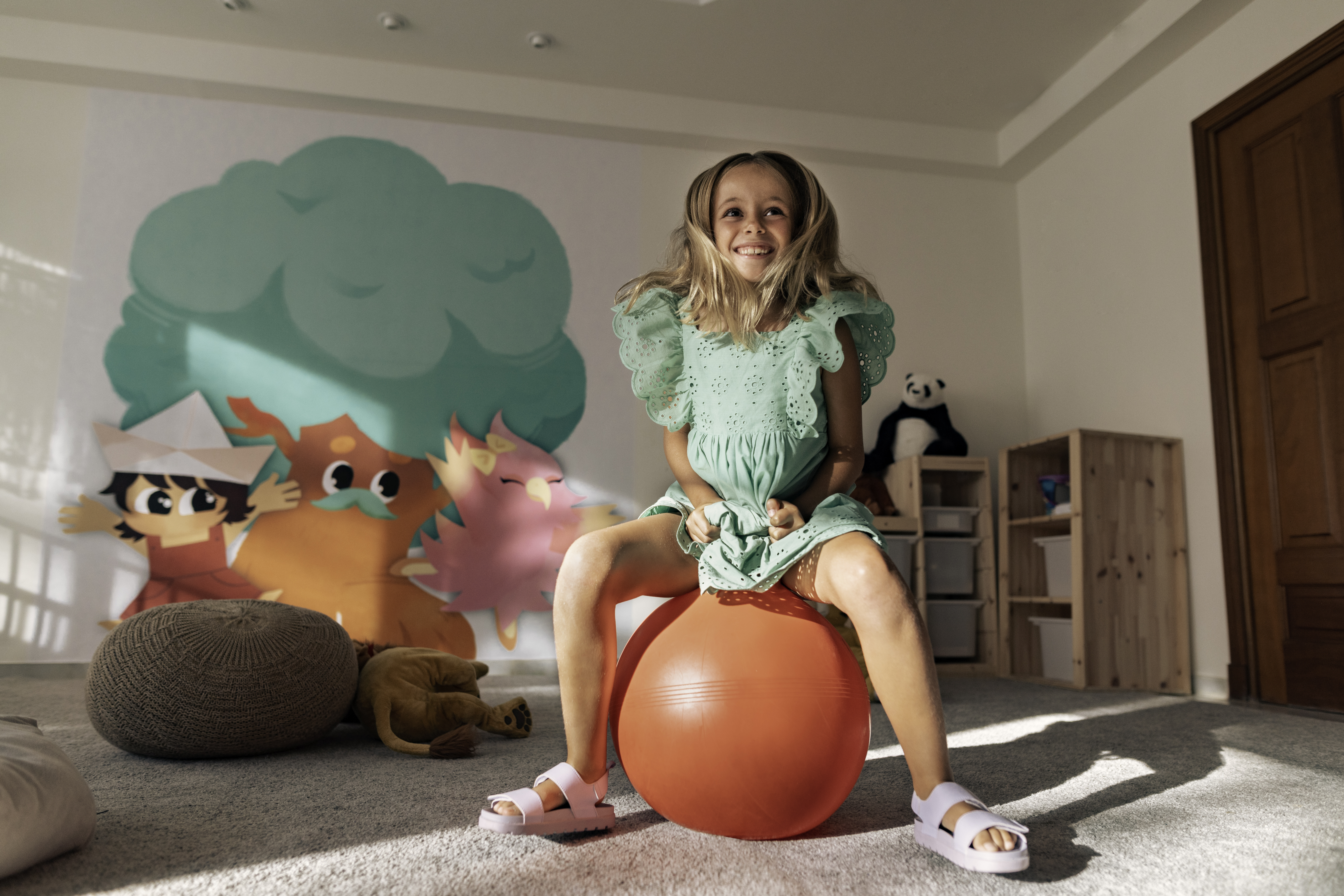 Smiling girl on red space hopper in bright playroom with colorful murals.