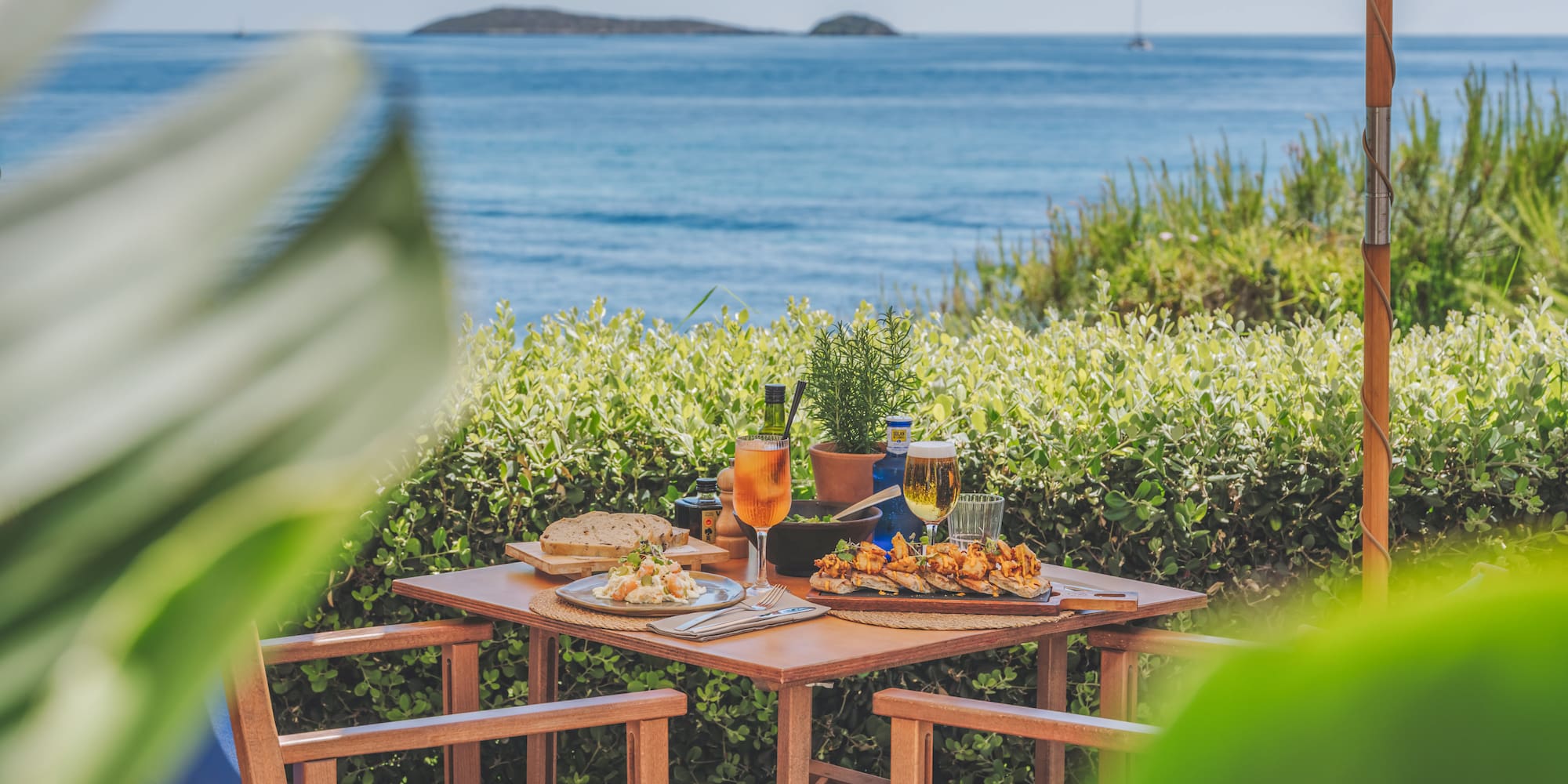 Beachfront restaurant table with Mediterranean food, aperitif, beer, and ocean view.