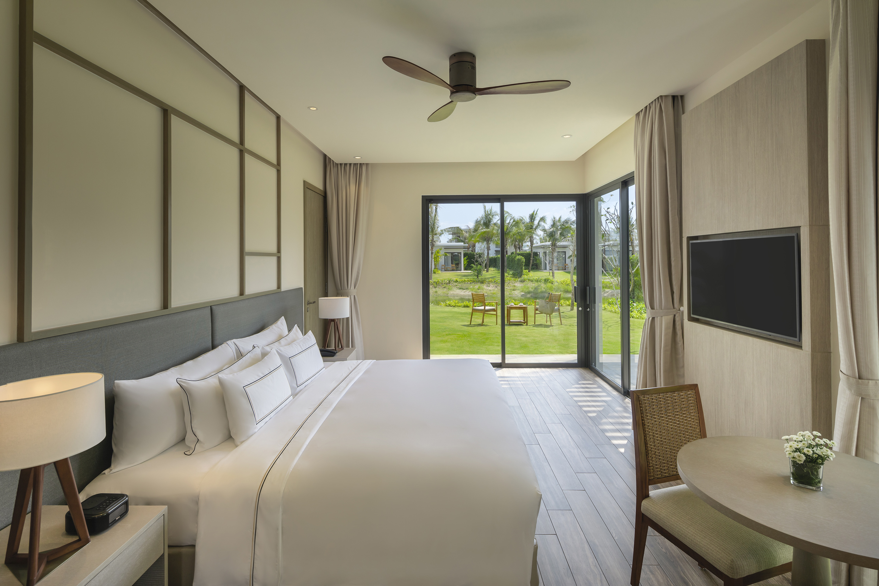 Modern hotel bedroom with king bed, garden view, and large glass doors.