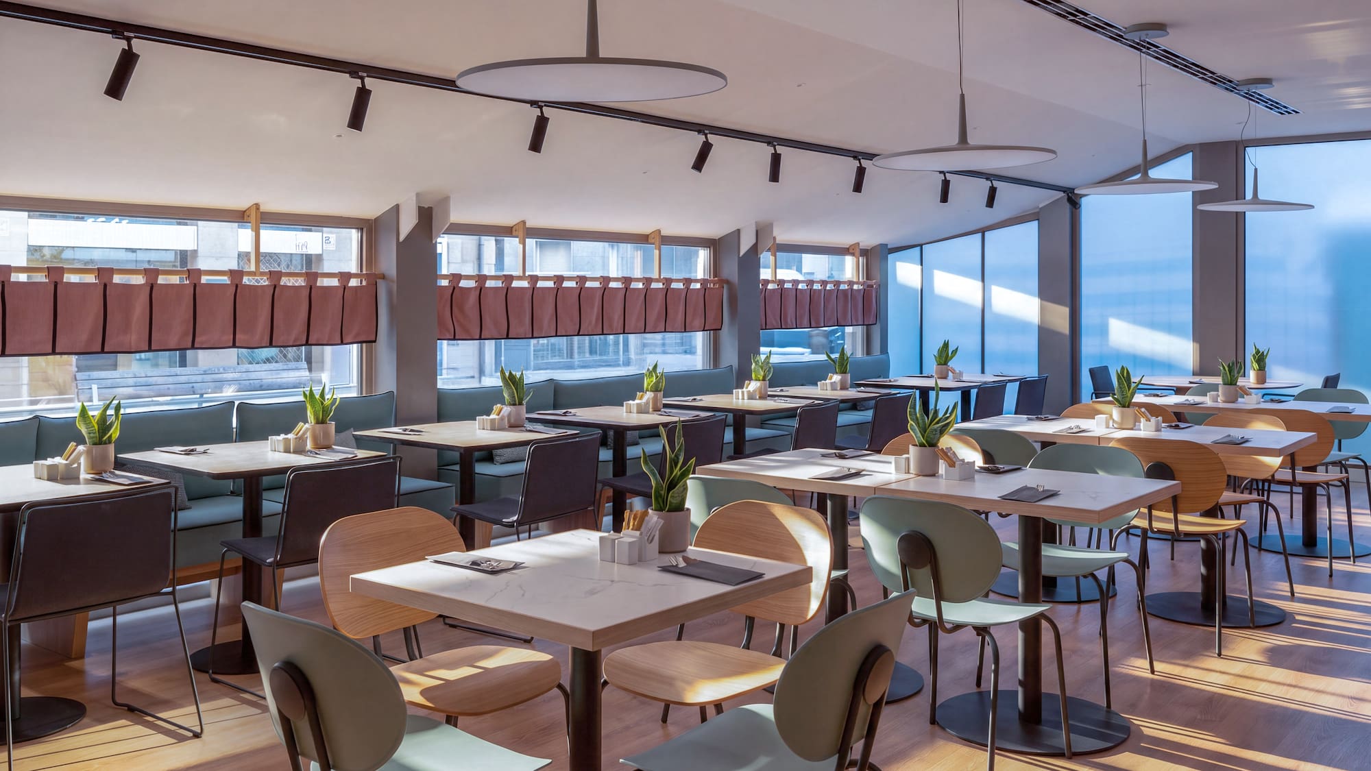 Cafetería moderna y luminosa con mesas, sillas variadas y plantas.