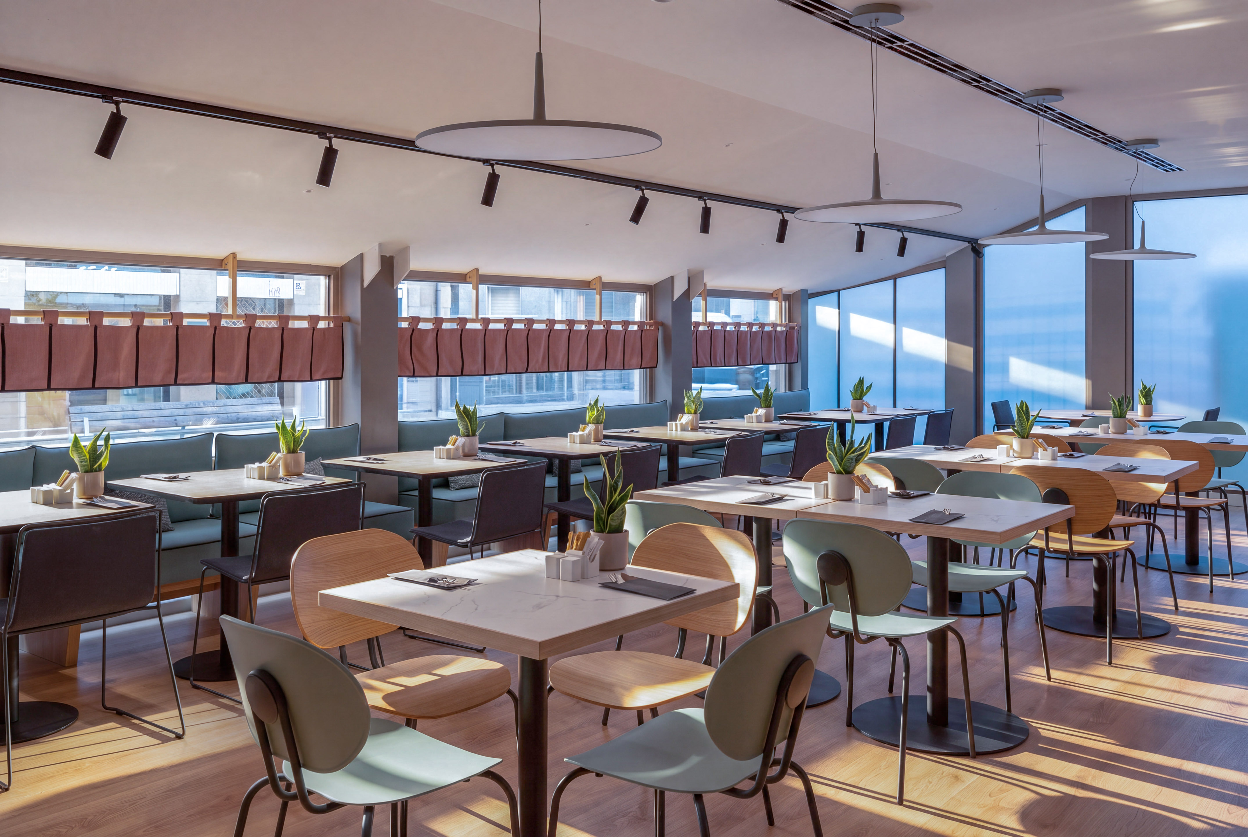 Cafetería moderna y luminosa con mesas, sillas variadas y plantas.