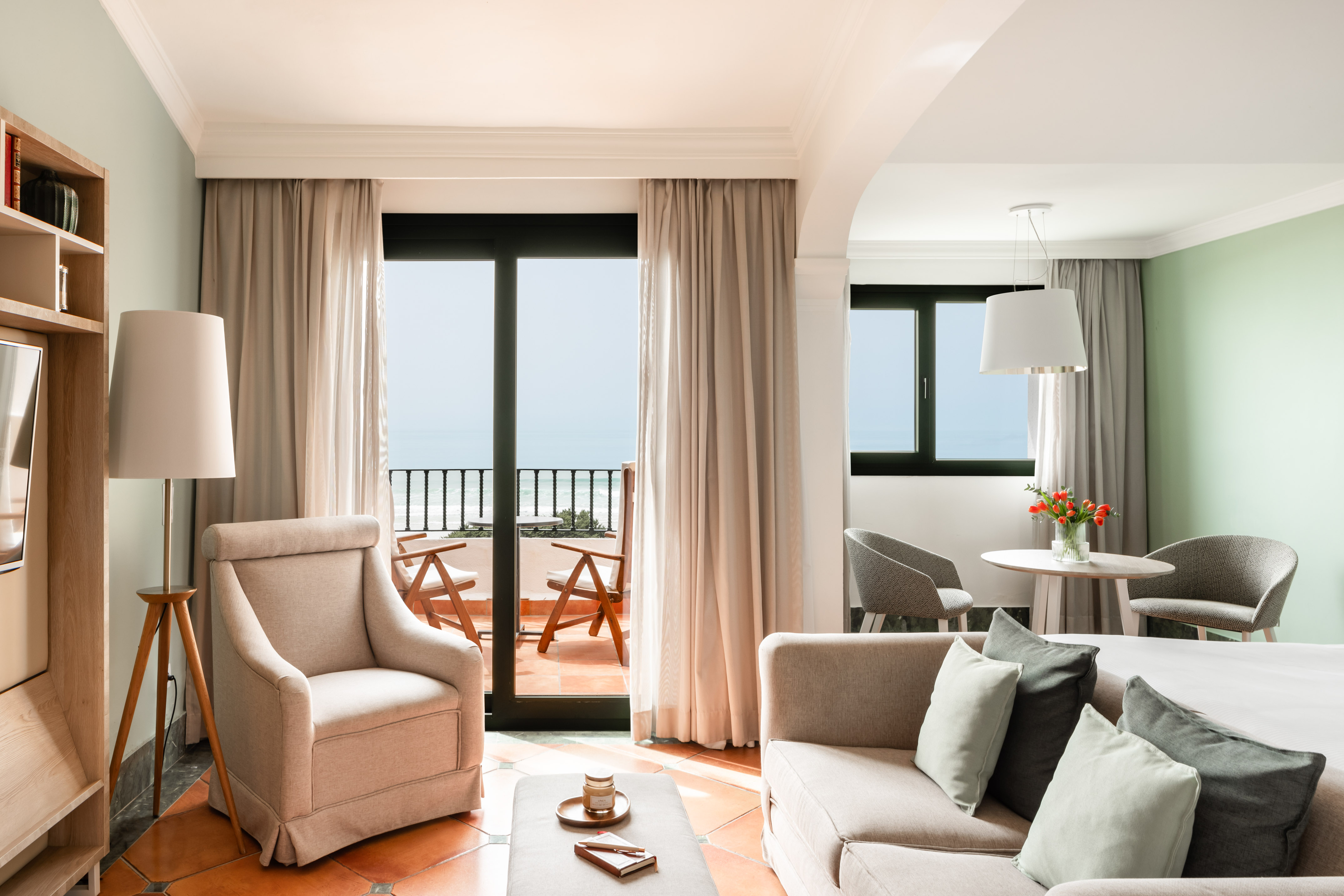 Hotel suite with ocean view balcony, living room, and modern furniture.