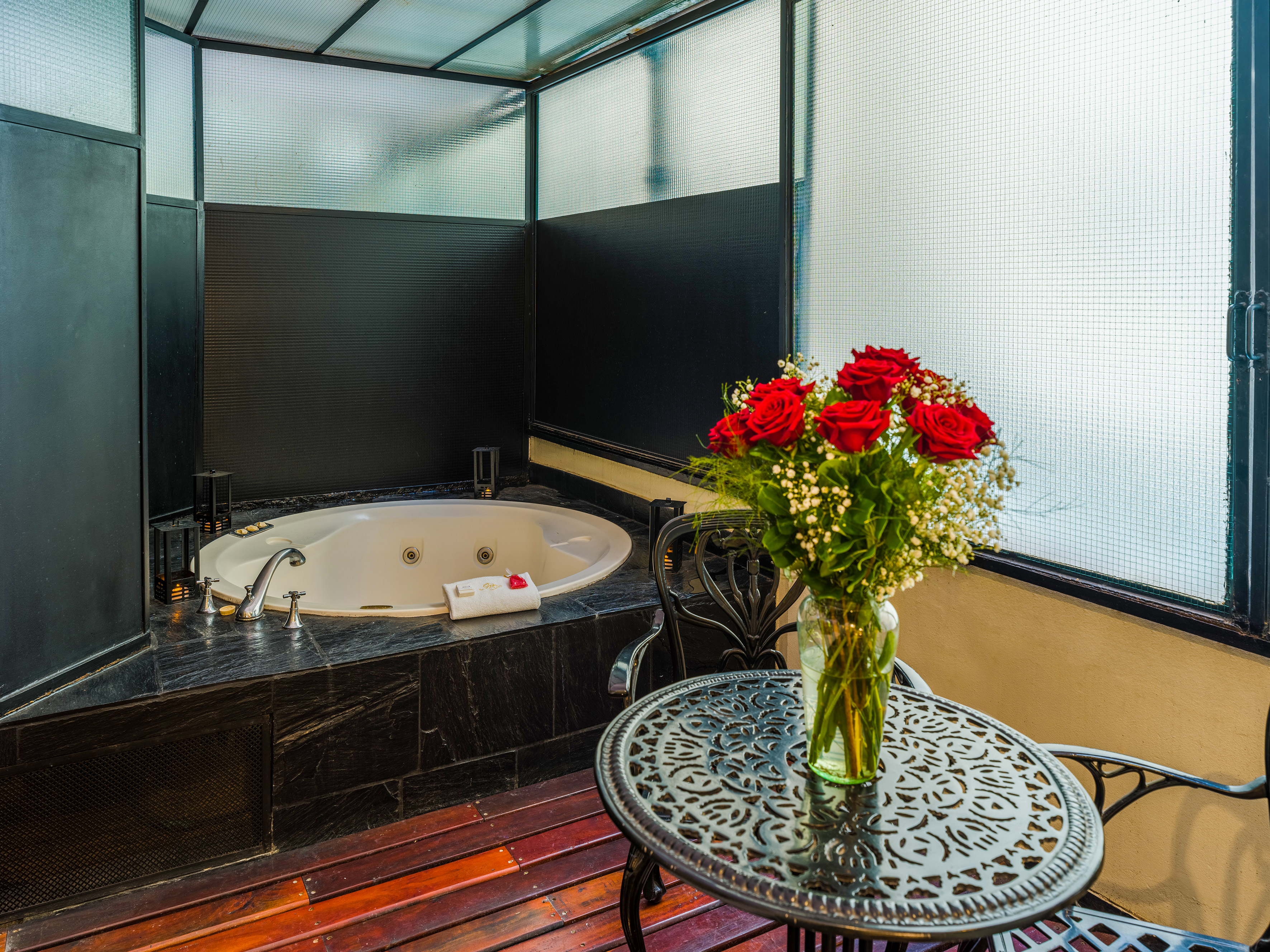 Luxury hot tub suite with red roses, ornate table, and wooden deck flooring.