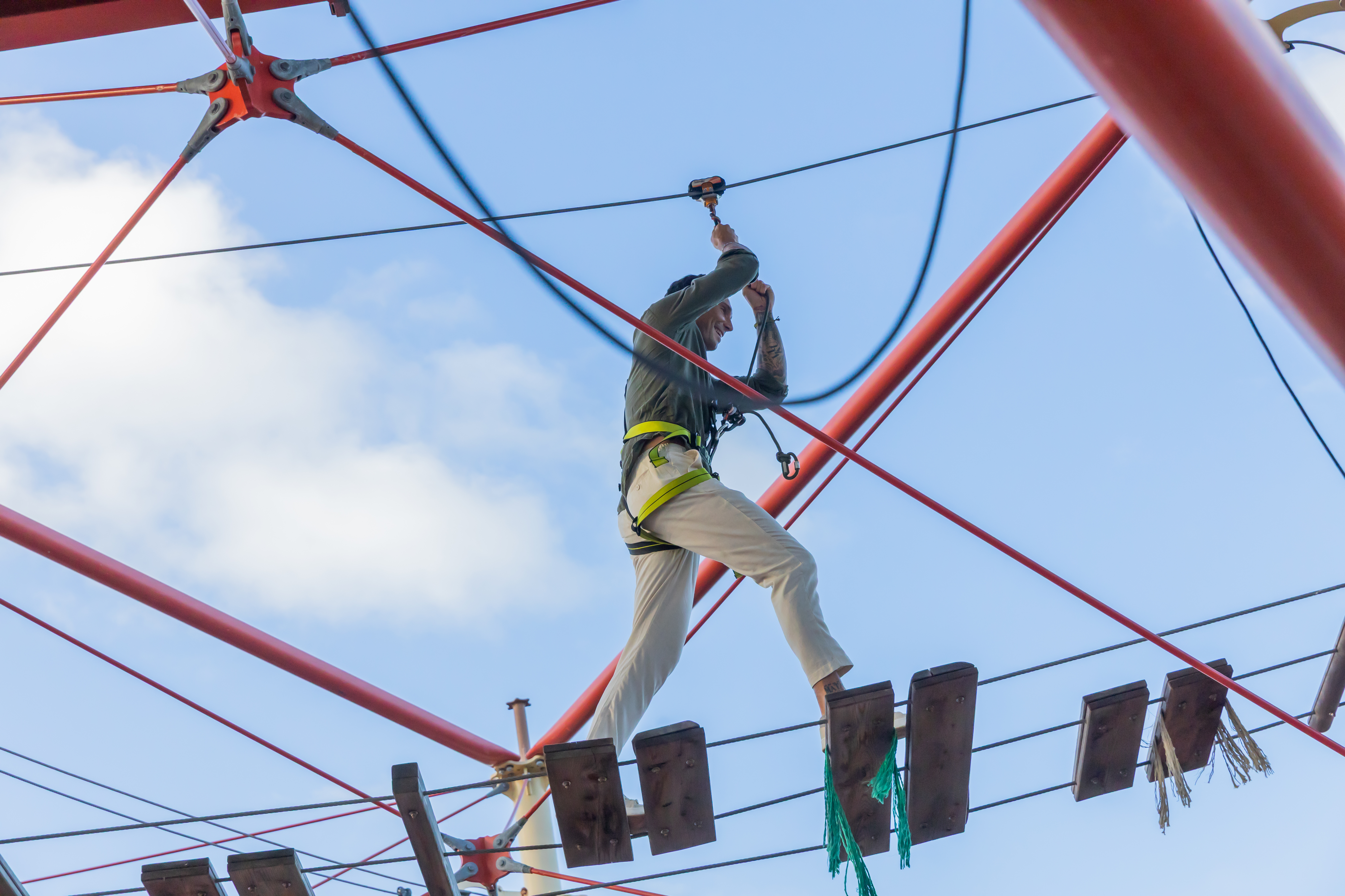 Man on high ropes course, balancing on planks with a safety harness.