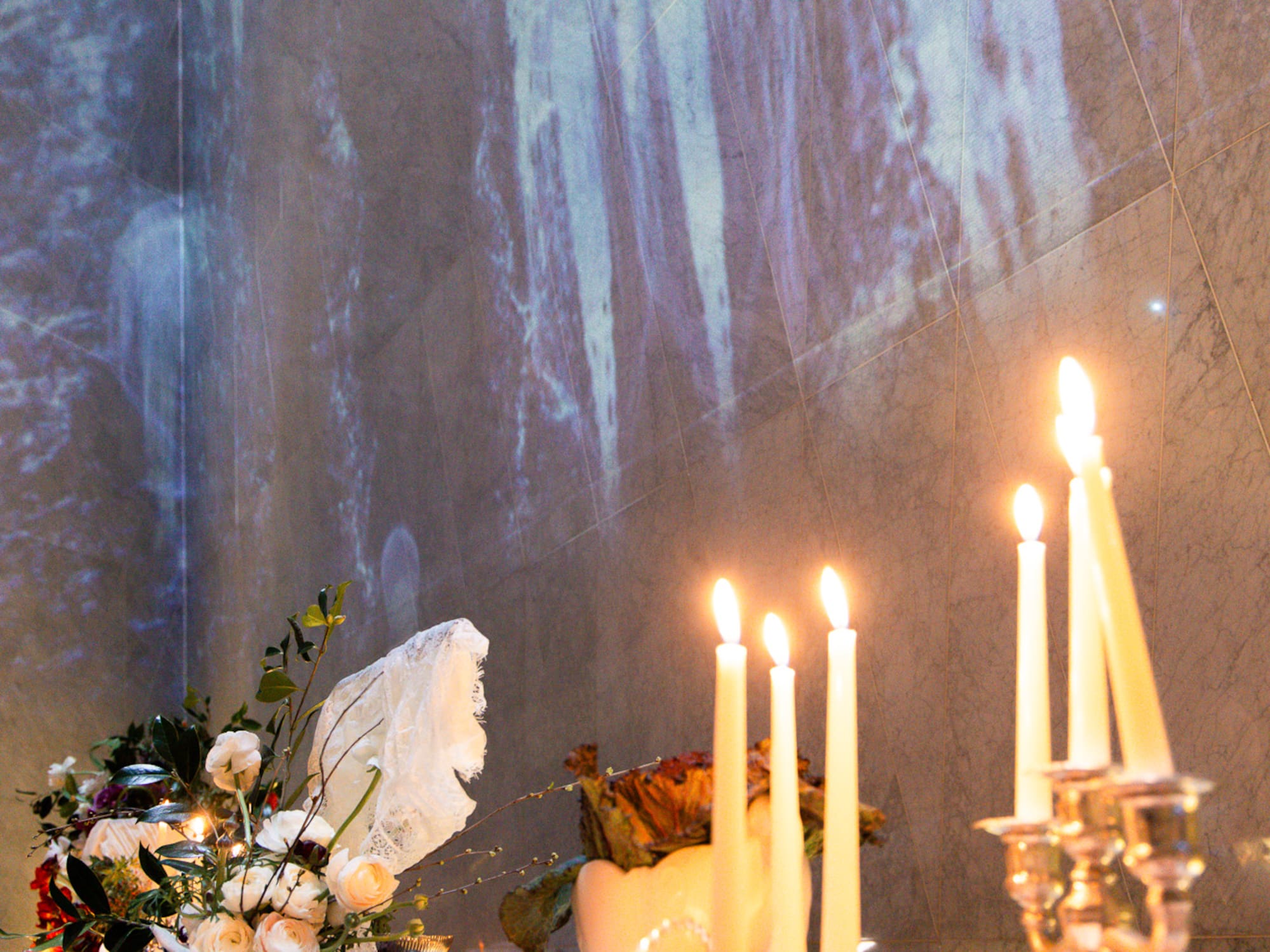 Candlelit table with flowers, fruit, and ambient wall projection.