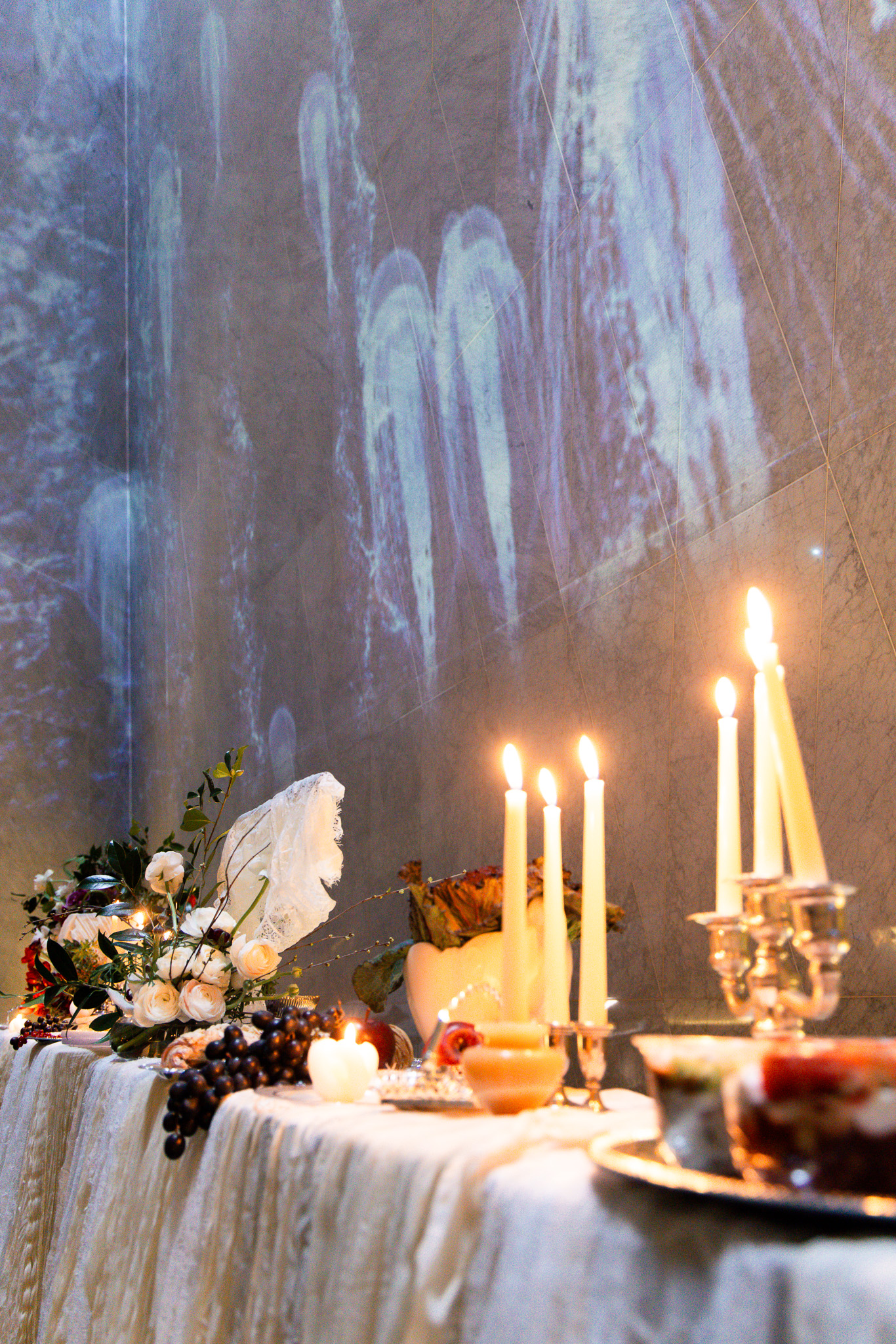 Candlelit table with flowers, fruit, and ambient wall projection.