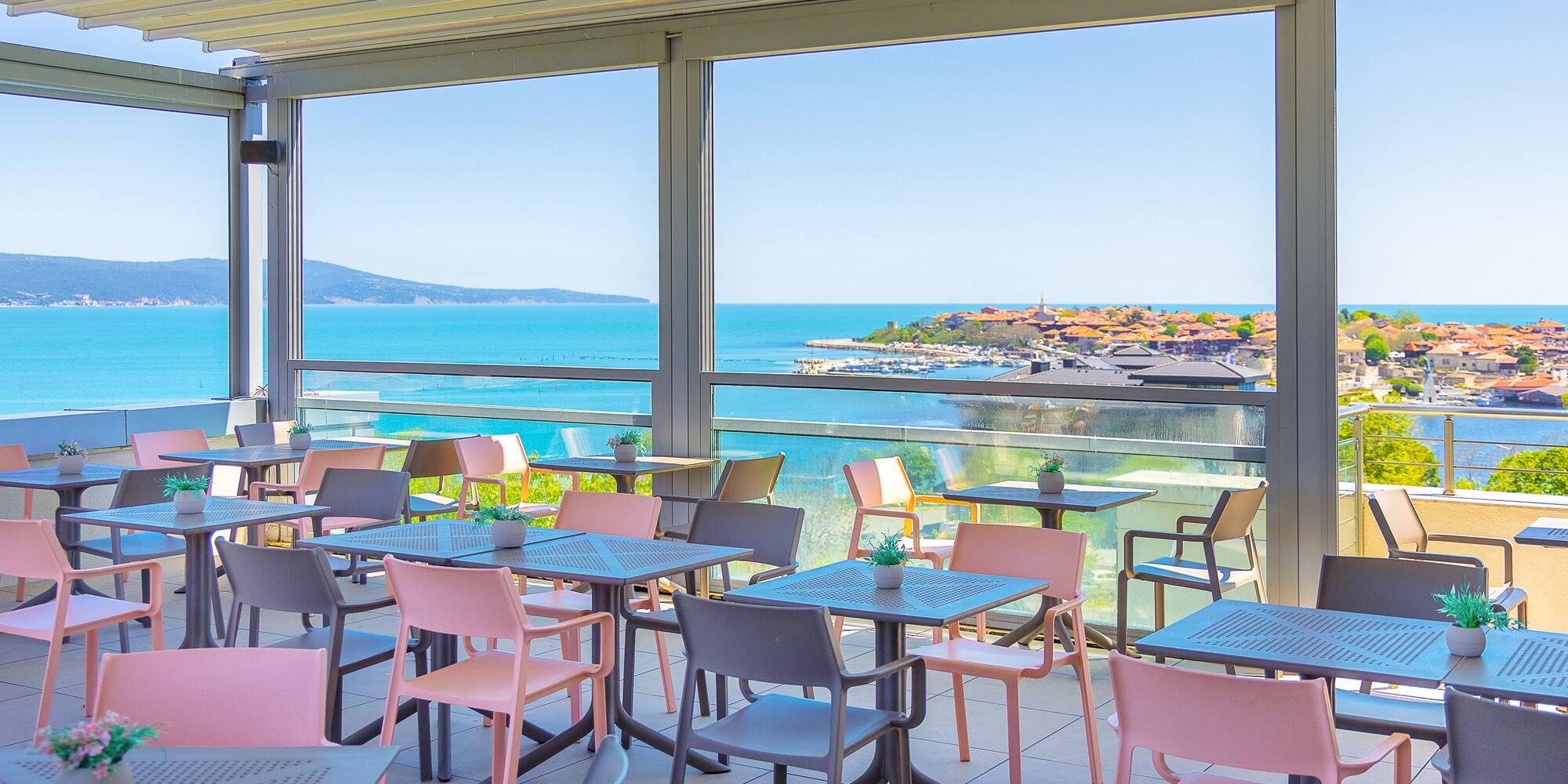 Outdoor dining terrace with coastal sea view and pink/grey chairs.