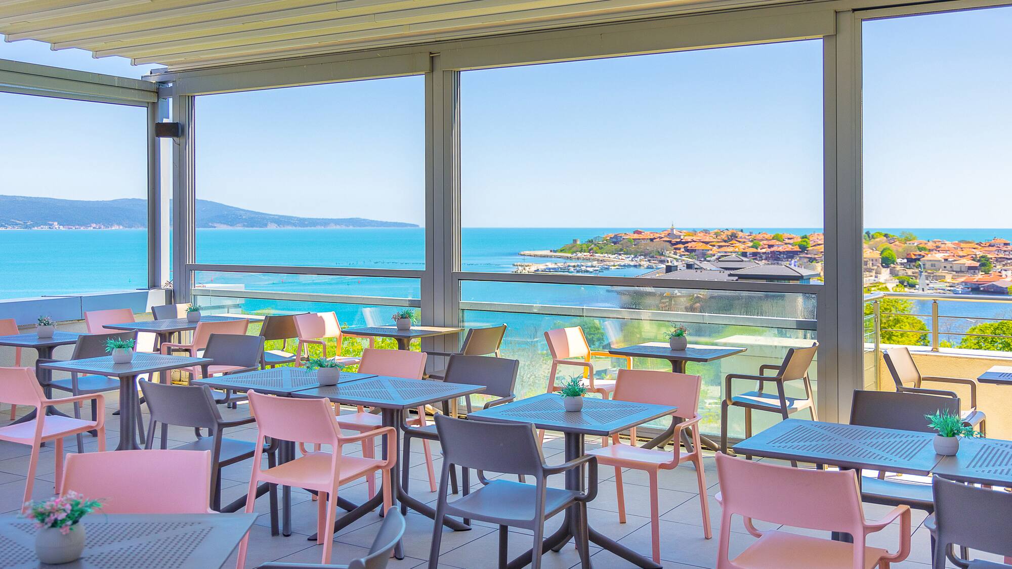 Outdoor dining terrace with coastal sea view and pink/grey chairs.