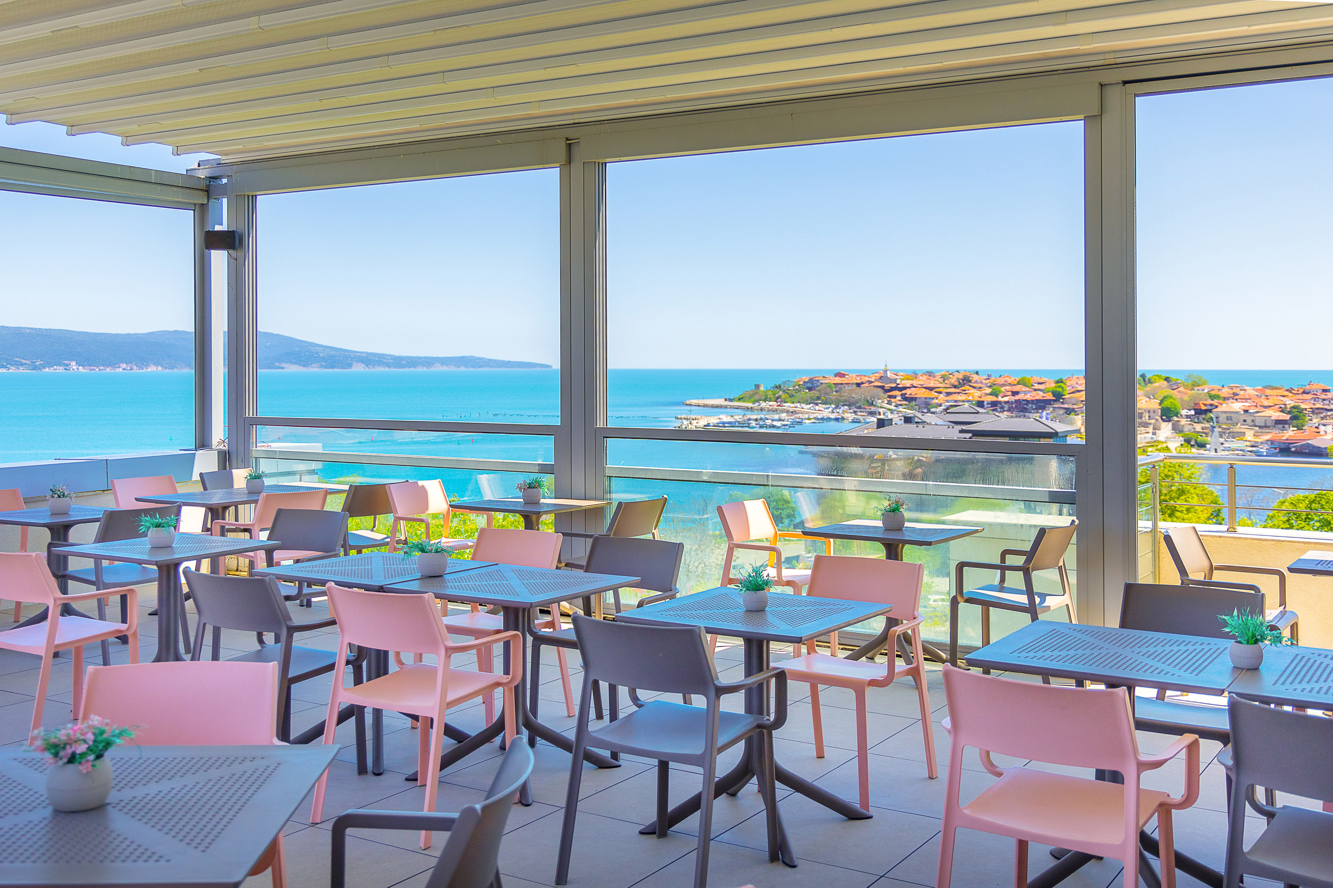 Outdoor dining terrace with coastal sea view and pink/grey chairs.