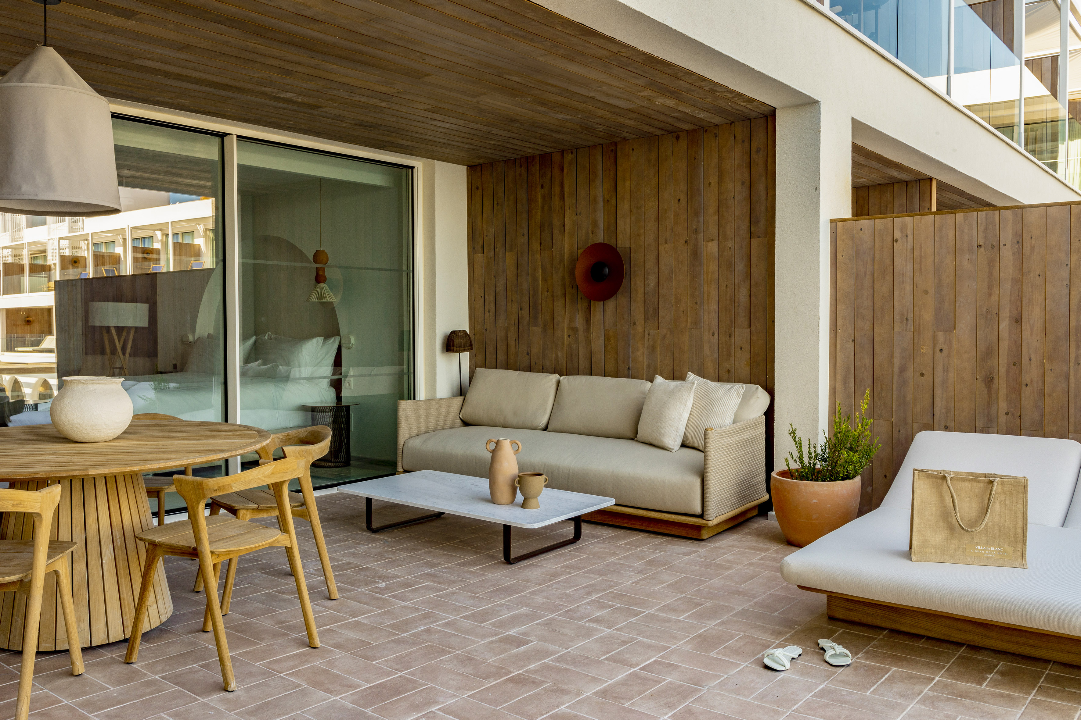 Outdoor luxury hotel patio with modern sofa, dining set, wood, and terracotta.