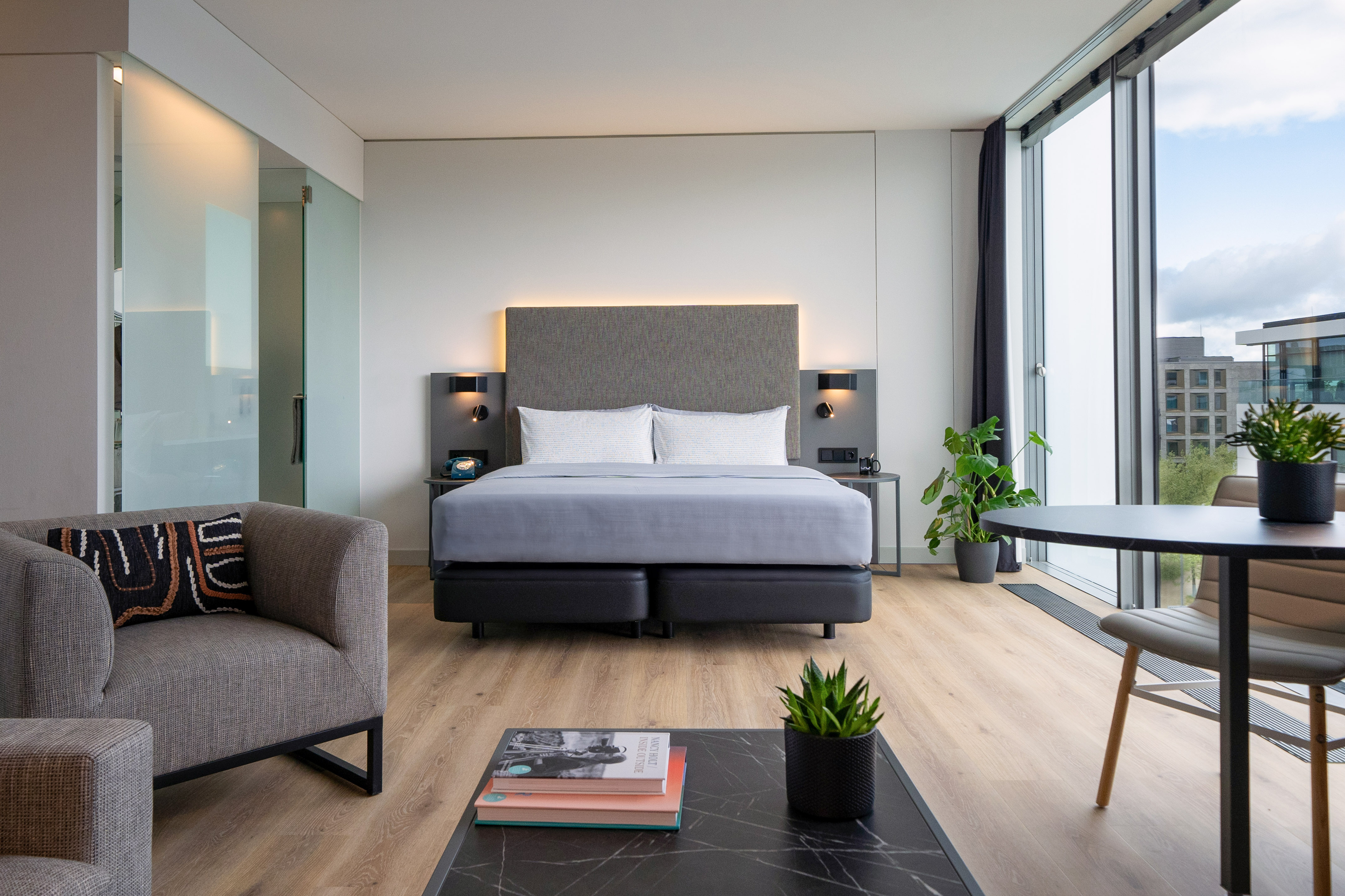 Contemporary hotel suite with king bed, sitting area, dining, and city view.