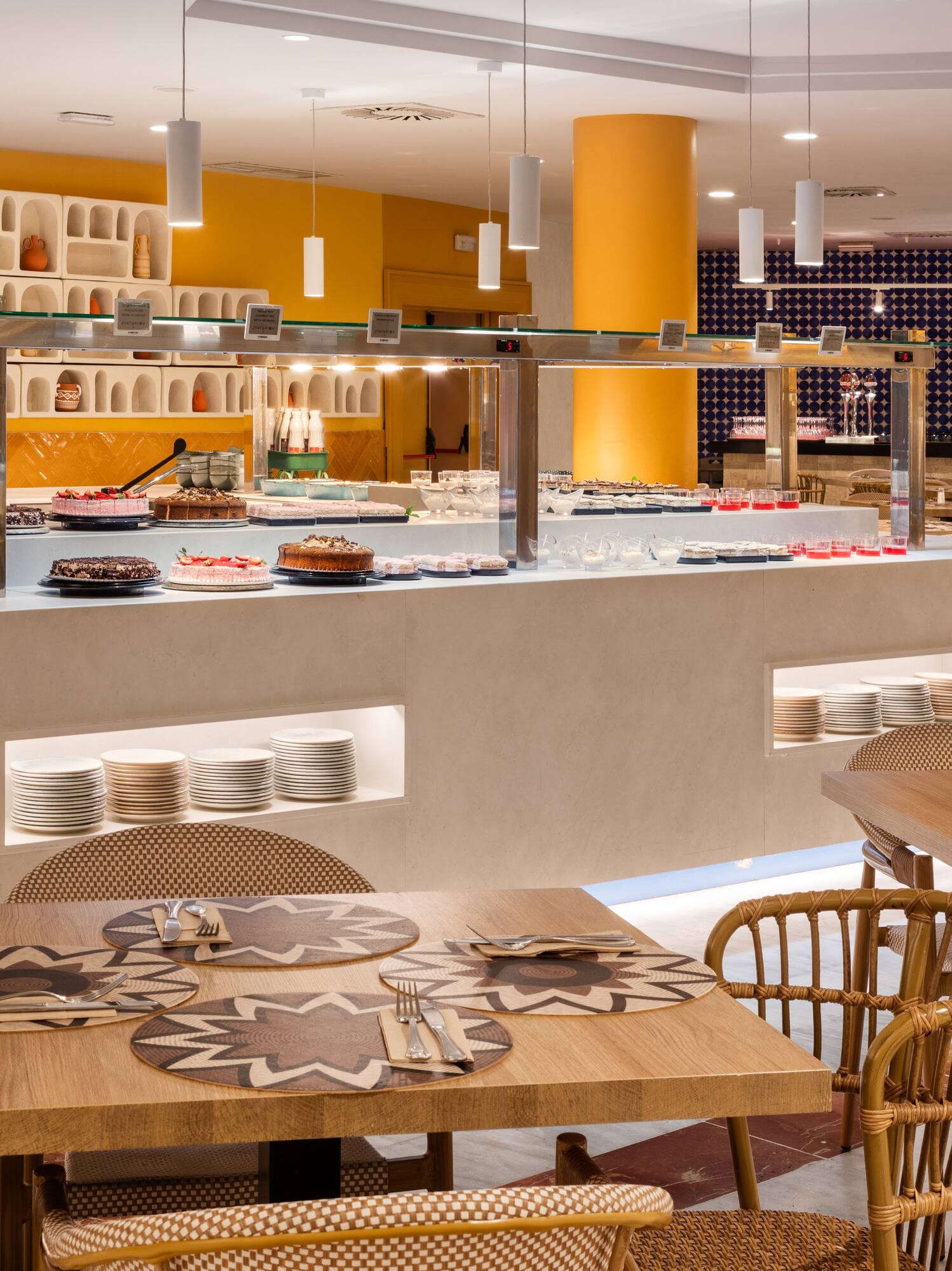 Bright modern buffet restaurant with dessert bar, fresh fruit, and wicker chairs.