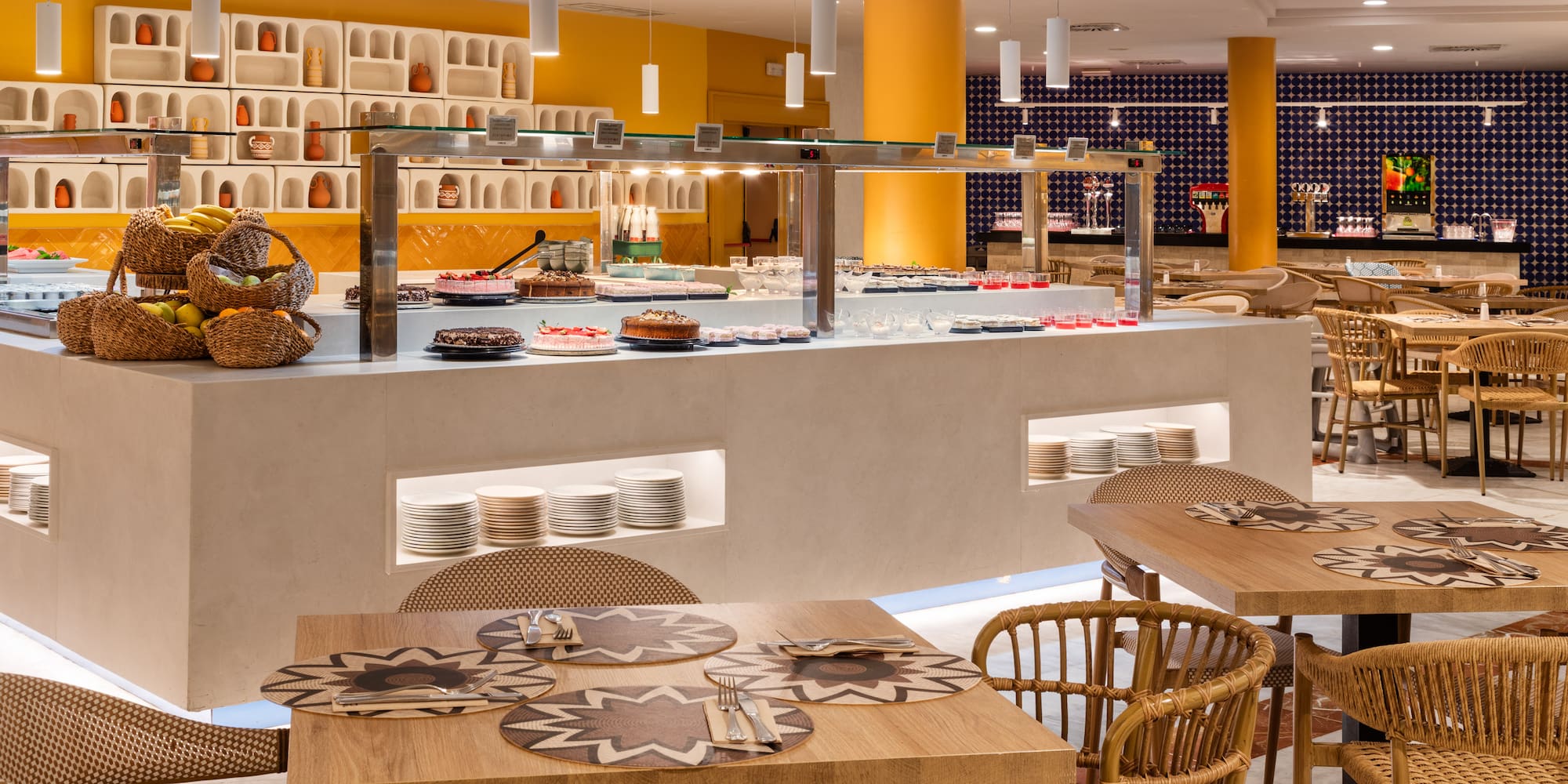 Bright hotel restaurant buffet with desserts, fruits, and modern dining tables.