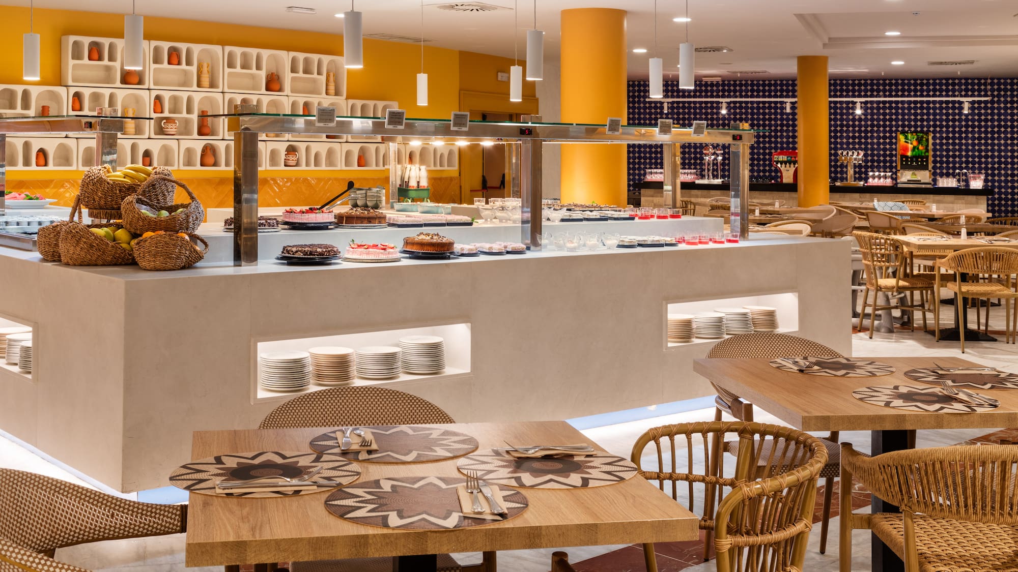 Bright hotel restaurant buffet with desserts, fruits, and modern dining tables.