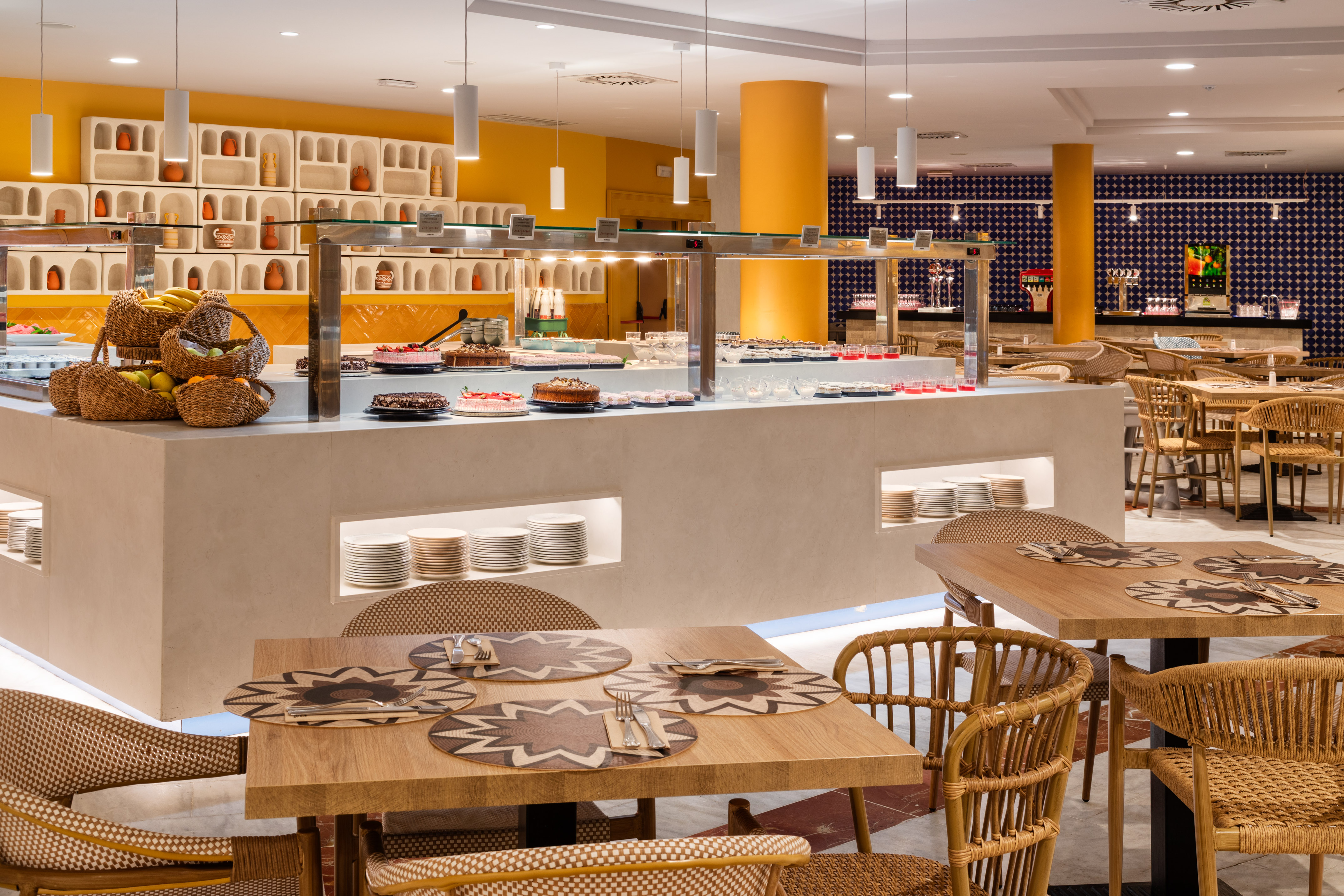 Bright modern buffet restaurant with dessert bar, fresh fruit, and wicker chairs.