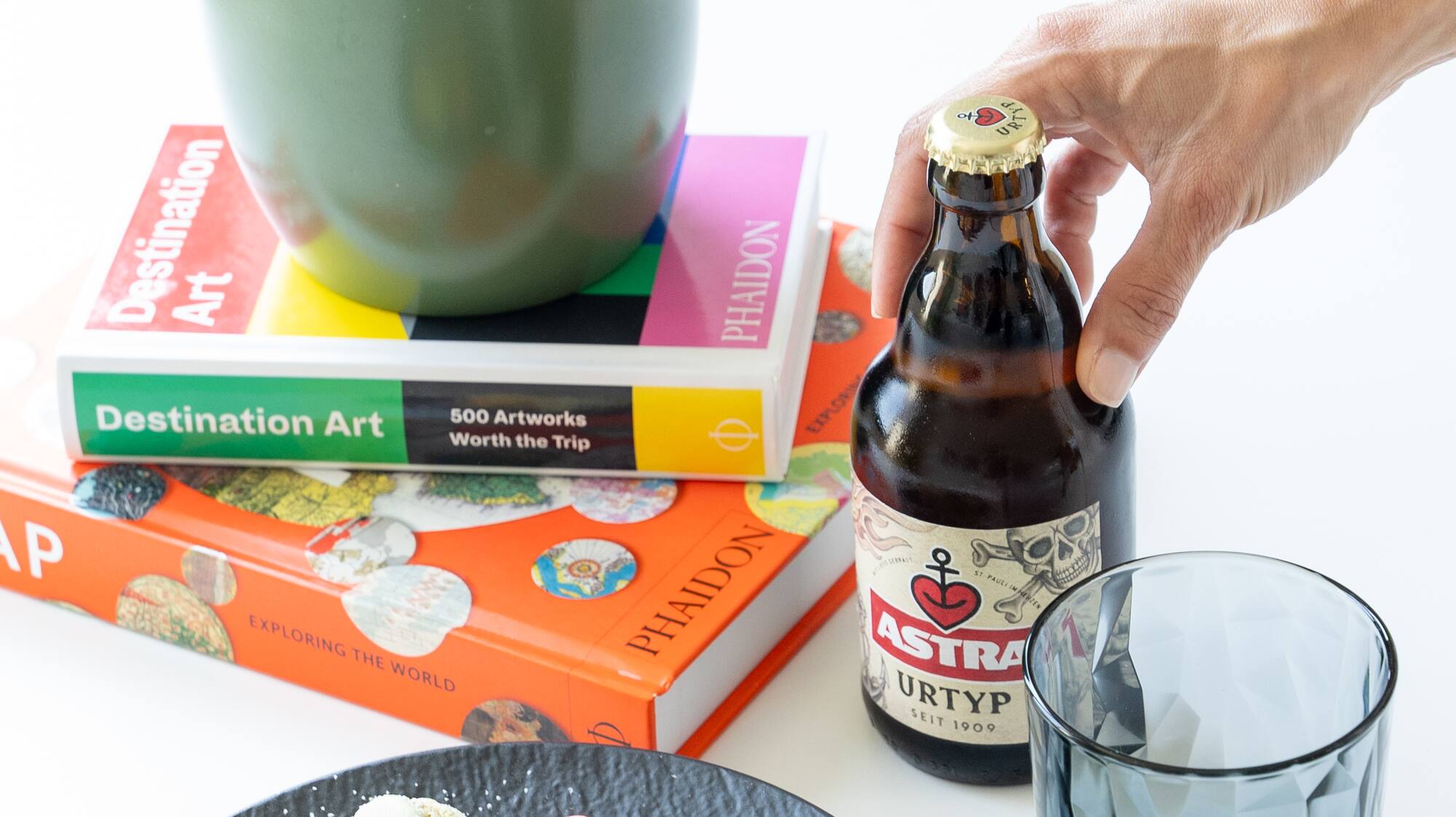 a hand holding a bottle of beer next to a plate of food