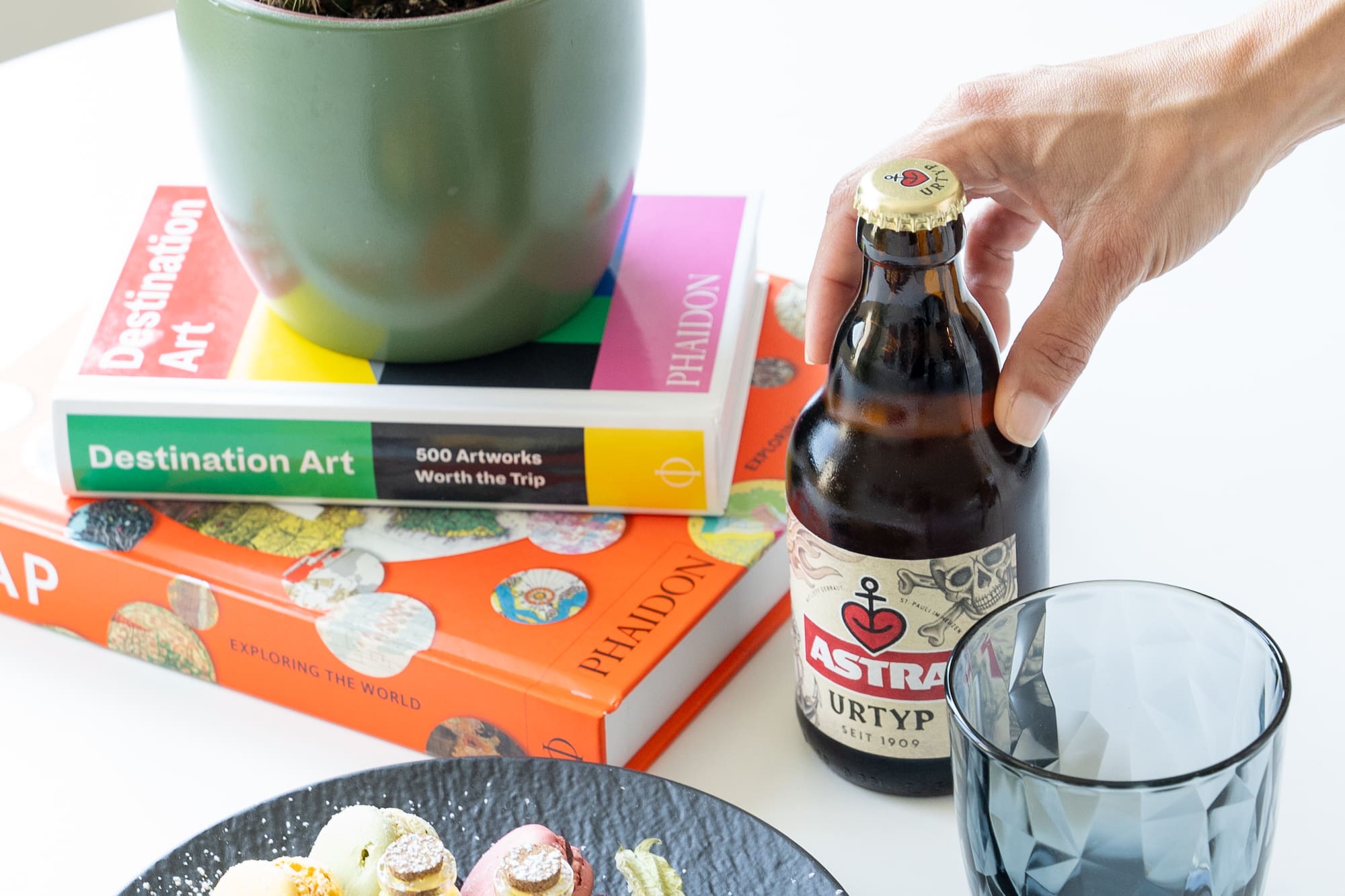 a hand holding a bottle of beer next to a plate of food