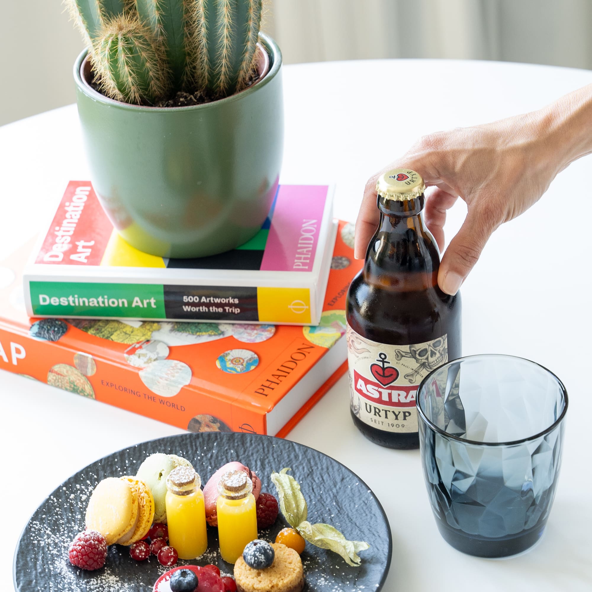 a hand holding a bottle of beer next to a plate of food