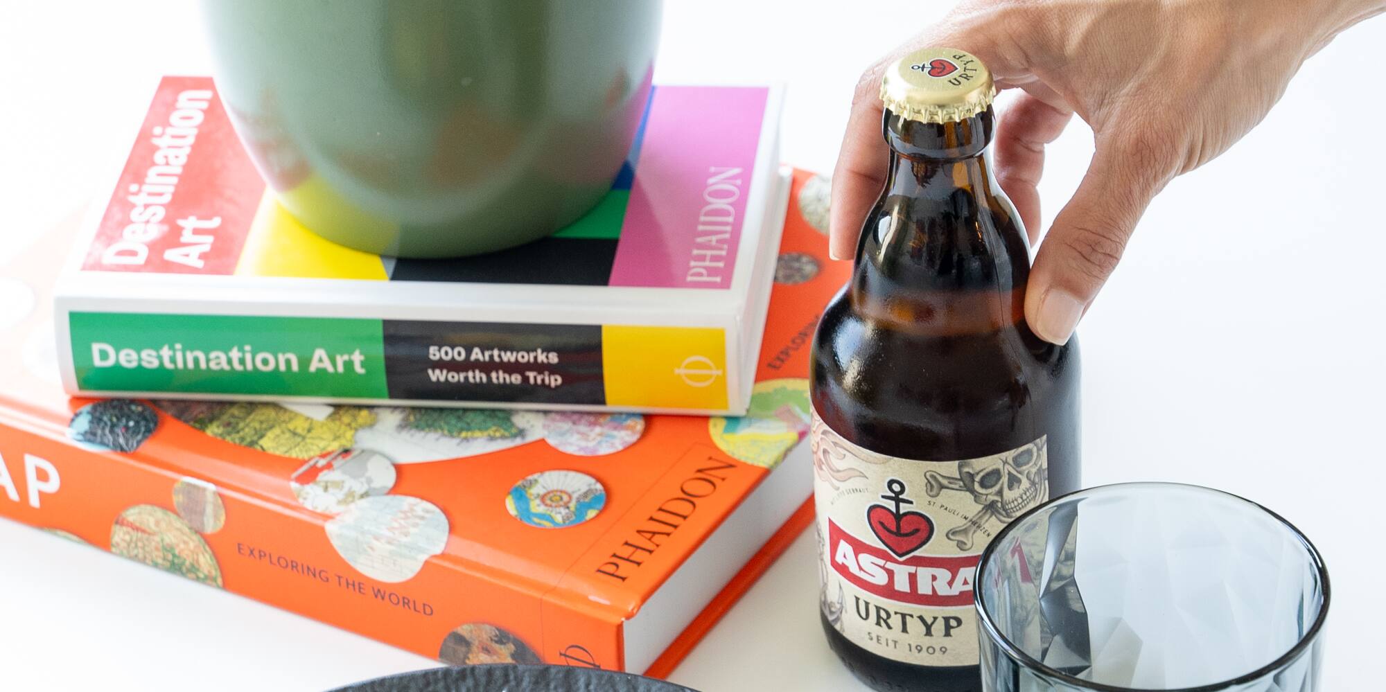 a hand holding a bottle of beer next to a plate of food