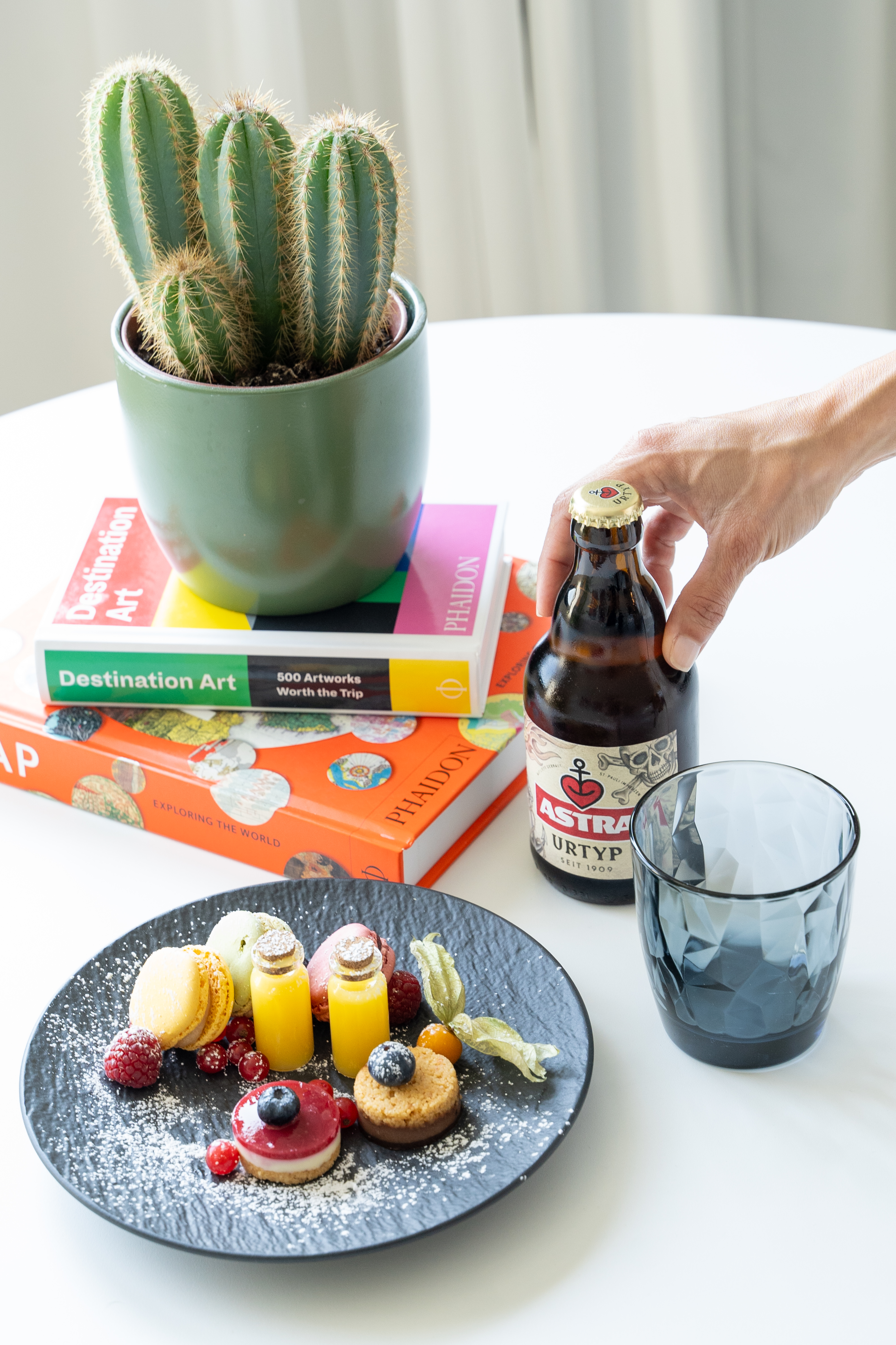 Assorted desserts, Astra beer, and cactus on coffee table books.