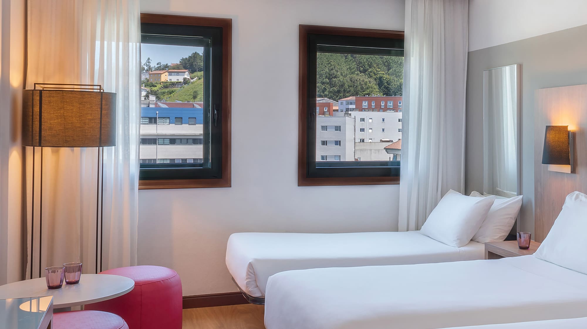 Bright triple hotel room with three single beds, city view, and wood floor.