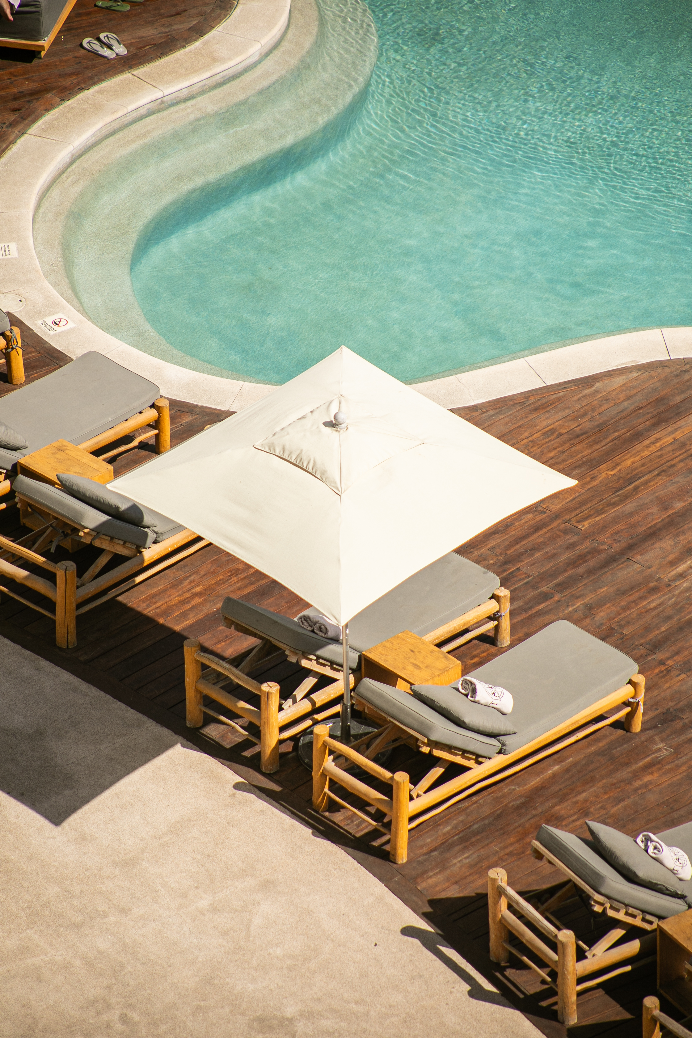 Luxury pool deck with sun loungers, white umbrella, and blue water.