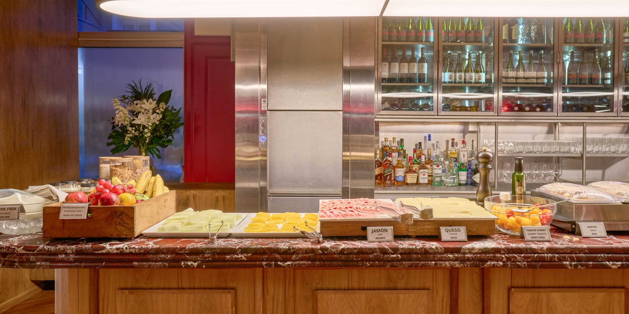 Hotel breakfast buffet featuring fresh fruit, ham, cheese, eggs, and drinks bar.