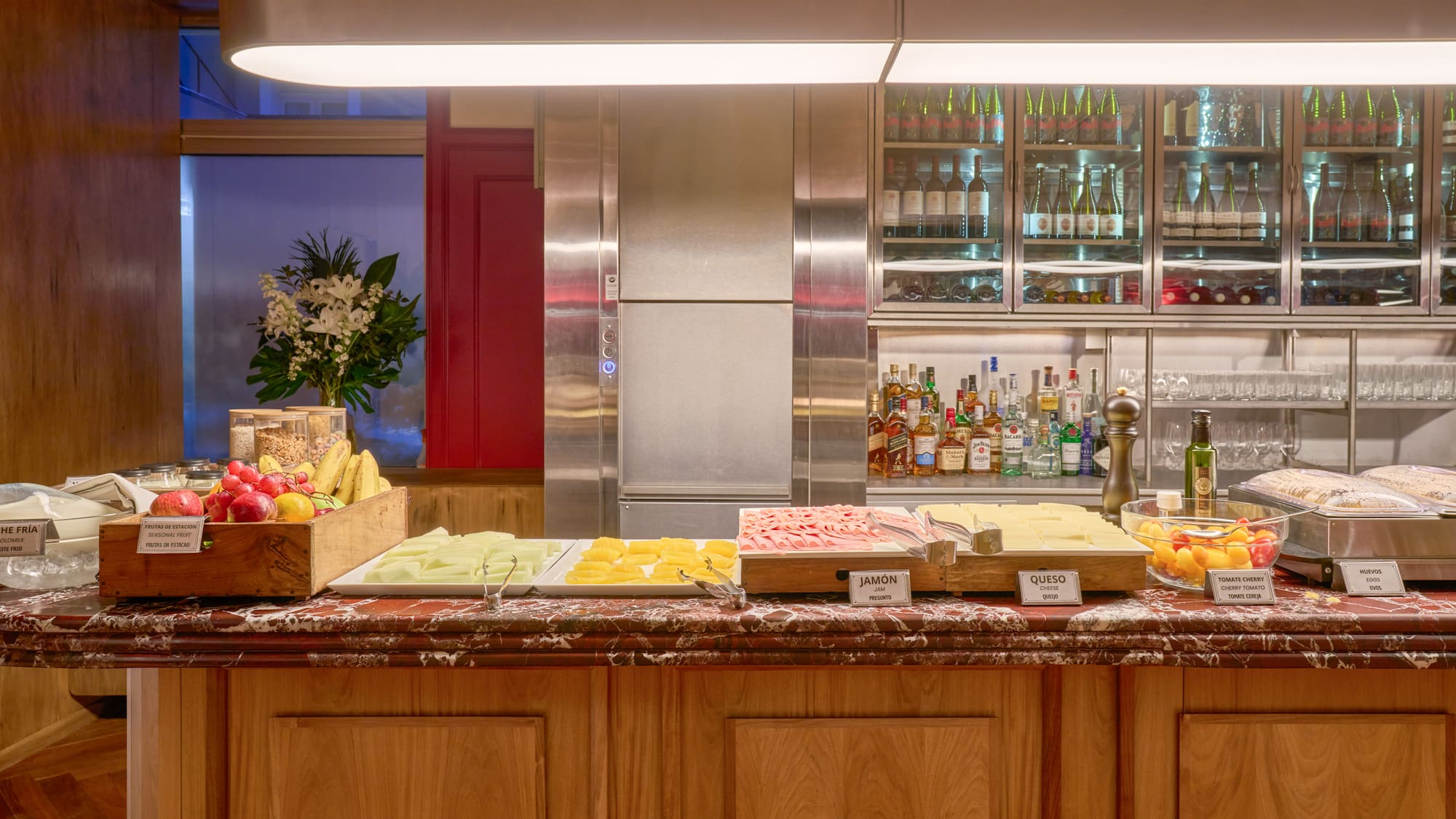 Hotel breakfast buffet featuring fresh fruit, ham, cheese, eggs, and drinks bar.