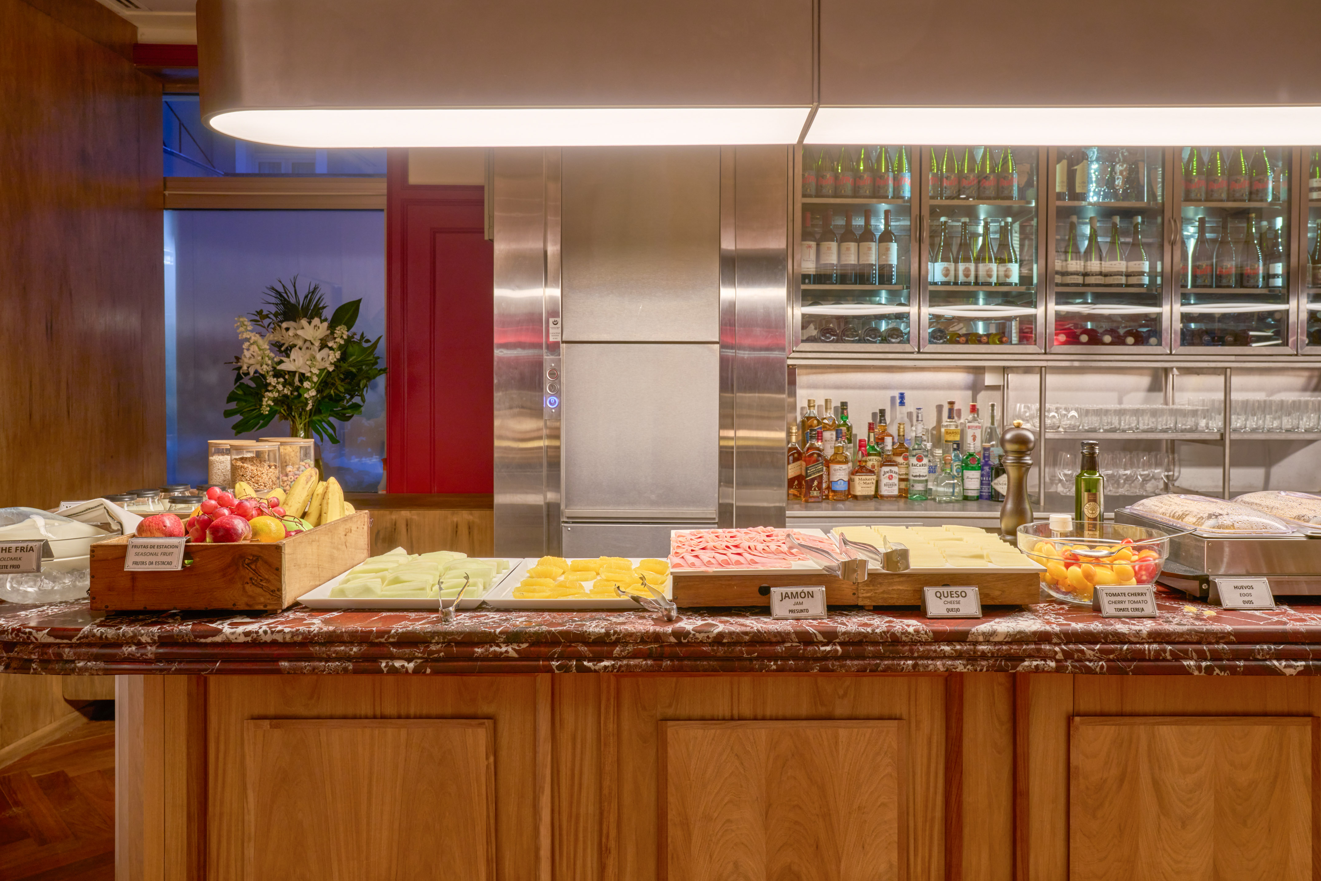 Hotel breakfast buffet featuring fresh fruit, ham, cheese, eggs, and drinks bar.