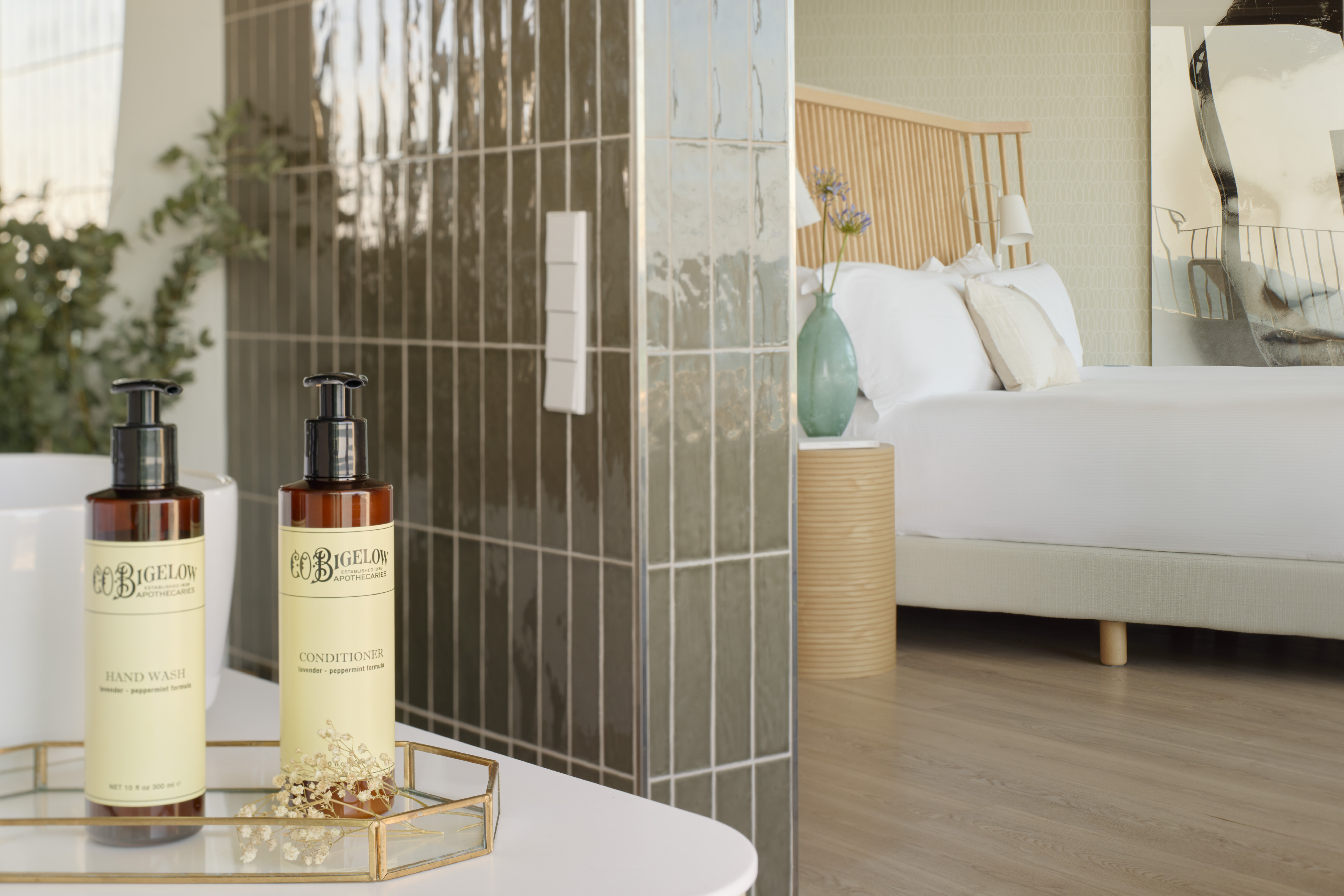Modern hotel bathroom with C.O. Bigelow amenities and bedroom view.