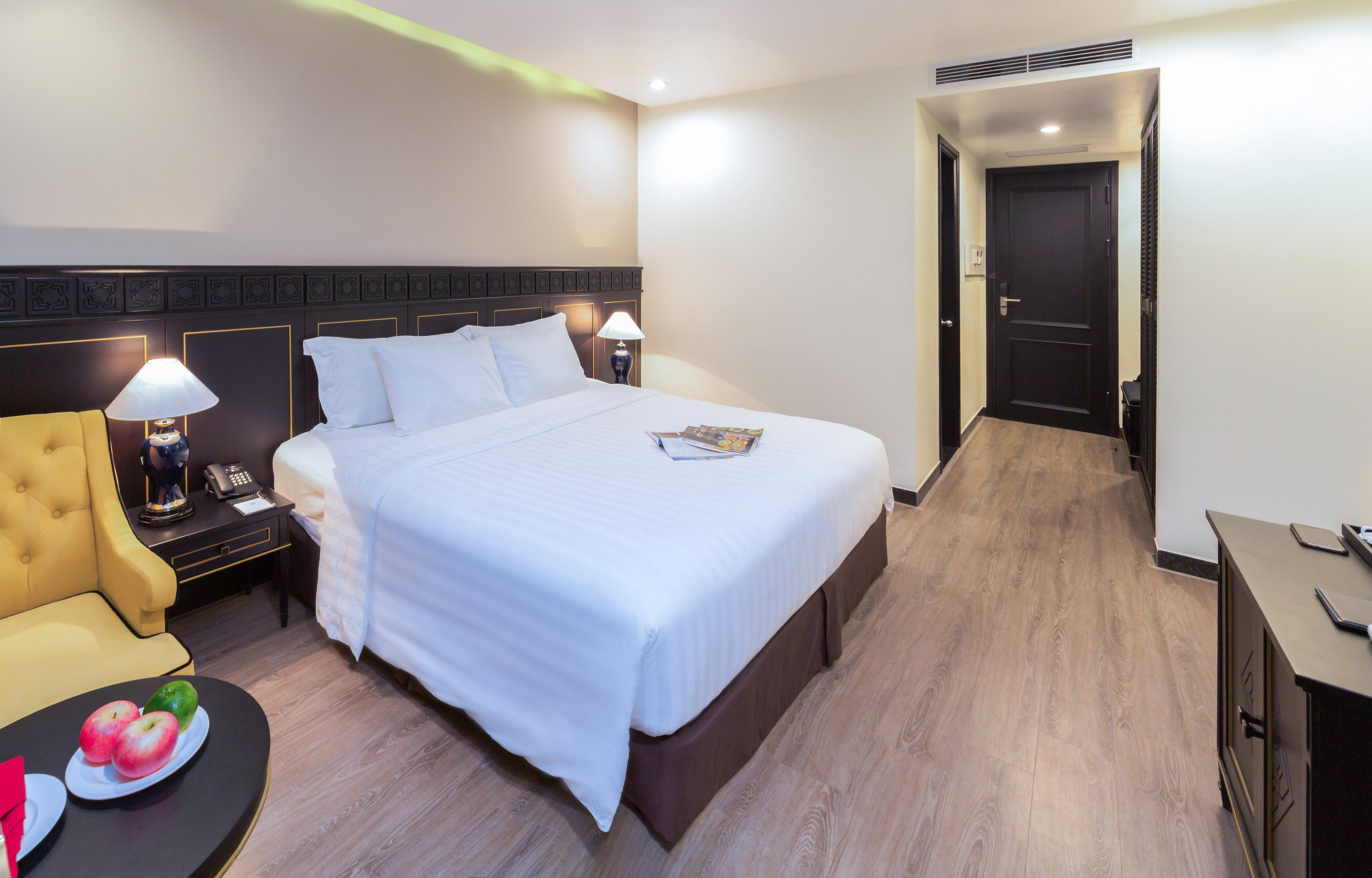 Hotel room with queen bed, dark headboard, yellow armchair, and wood floor.