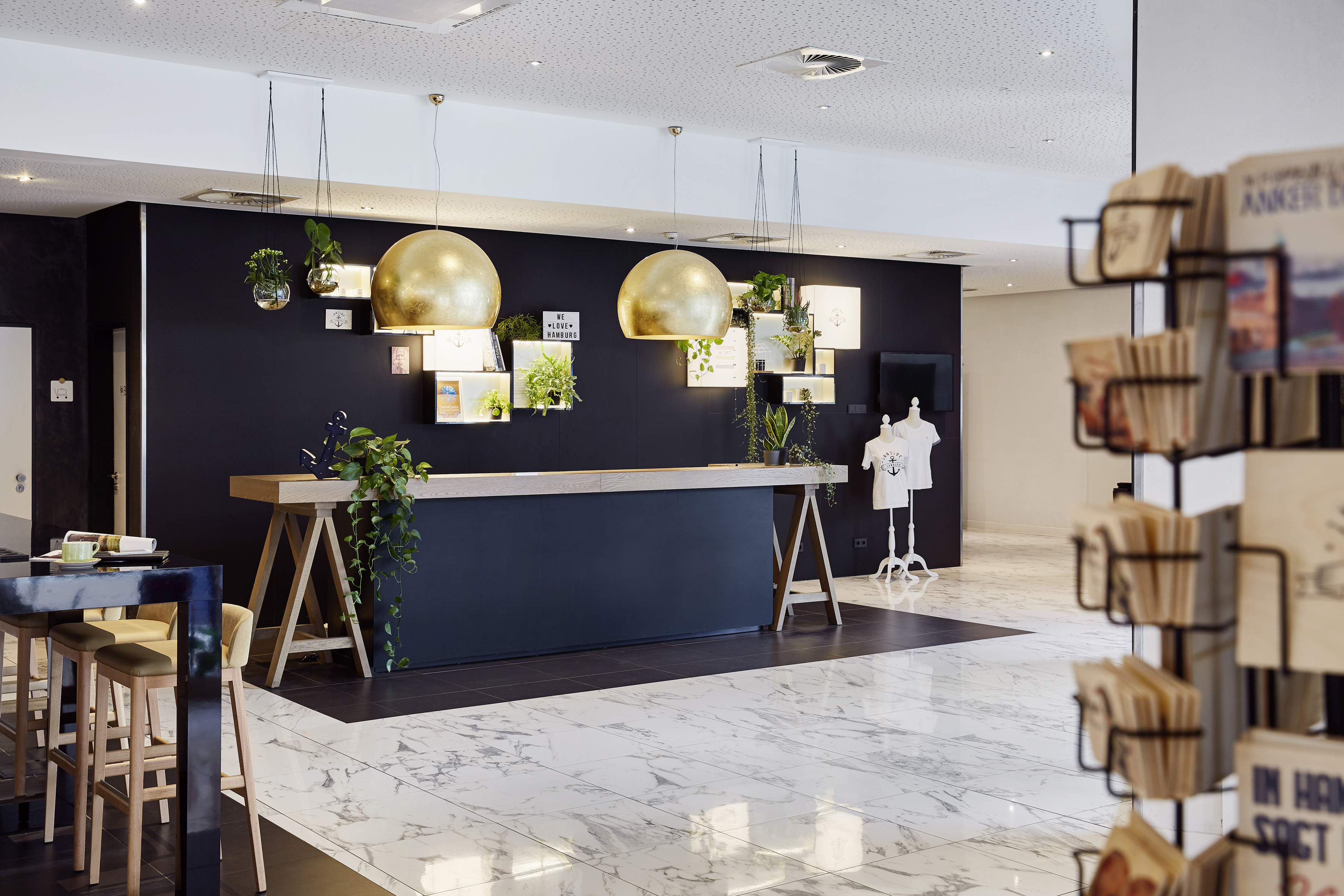 Modern hotel lobby with gold lights, reception desk, green plants, and marble floor.