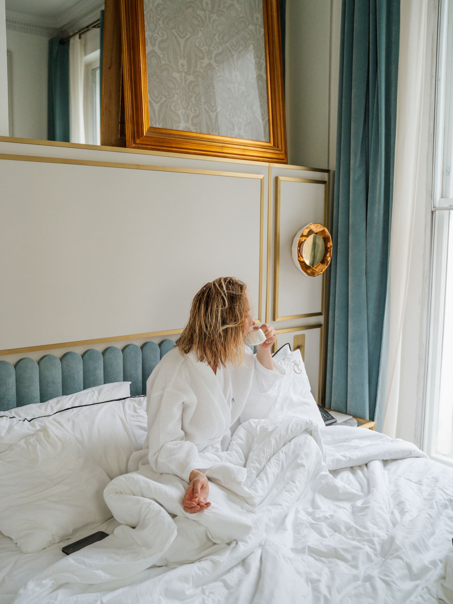 a woman sitting on a bed drinking from a cup