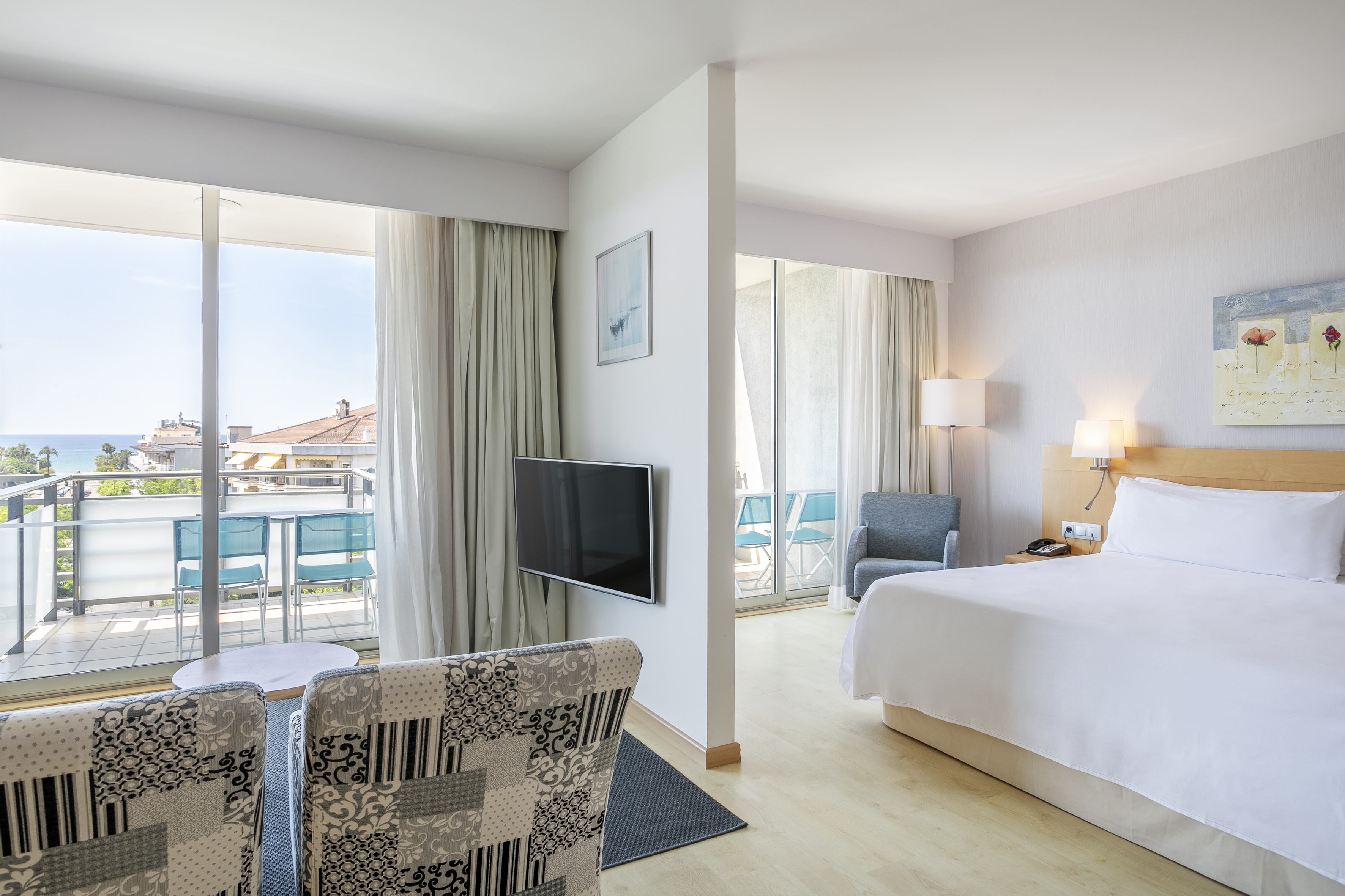 Modern hotel room with ocean view balcony, king bed, and living area.