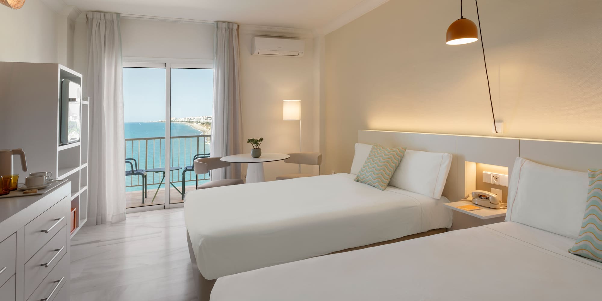 Habitación de hotel doble moderna con balcón y vistas al mar.