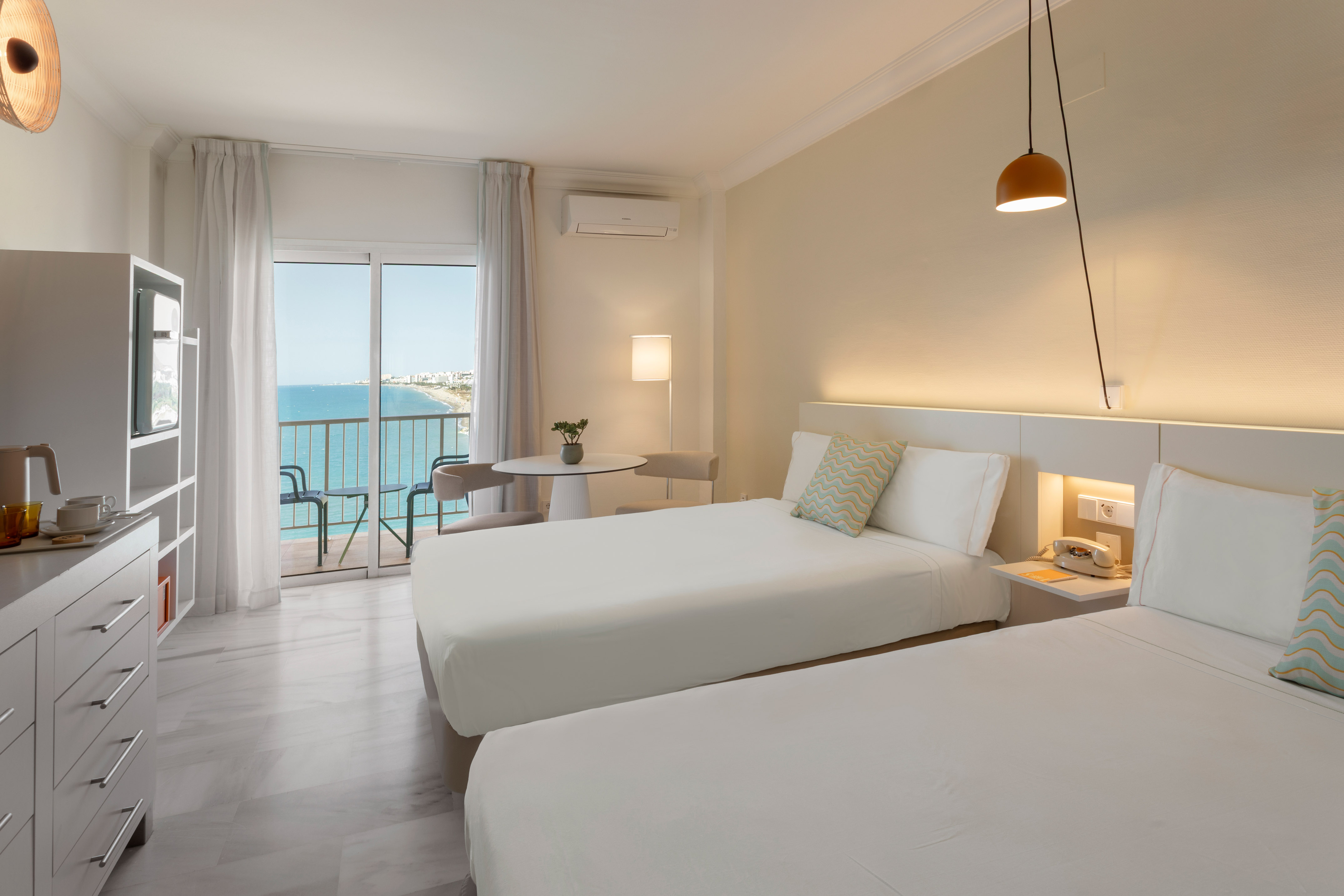 Habitación de hotel doble moderna con balcón y vistas al mar.