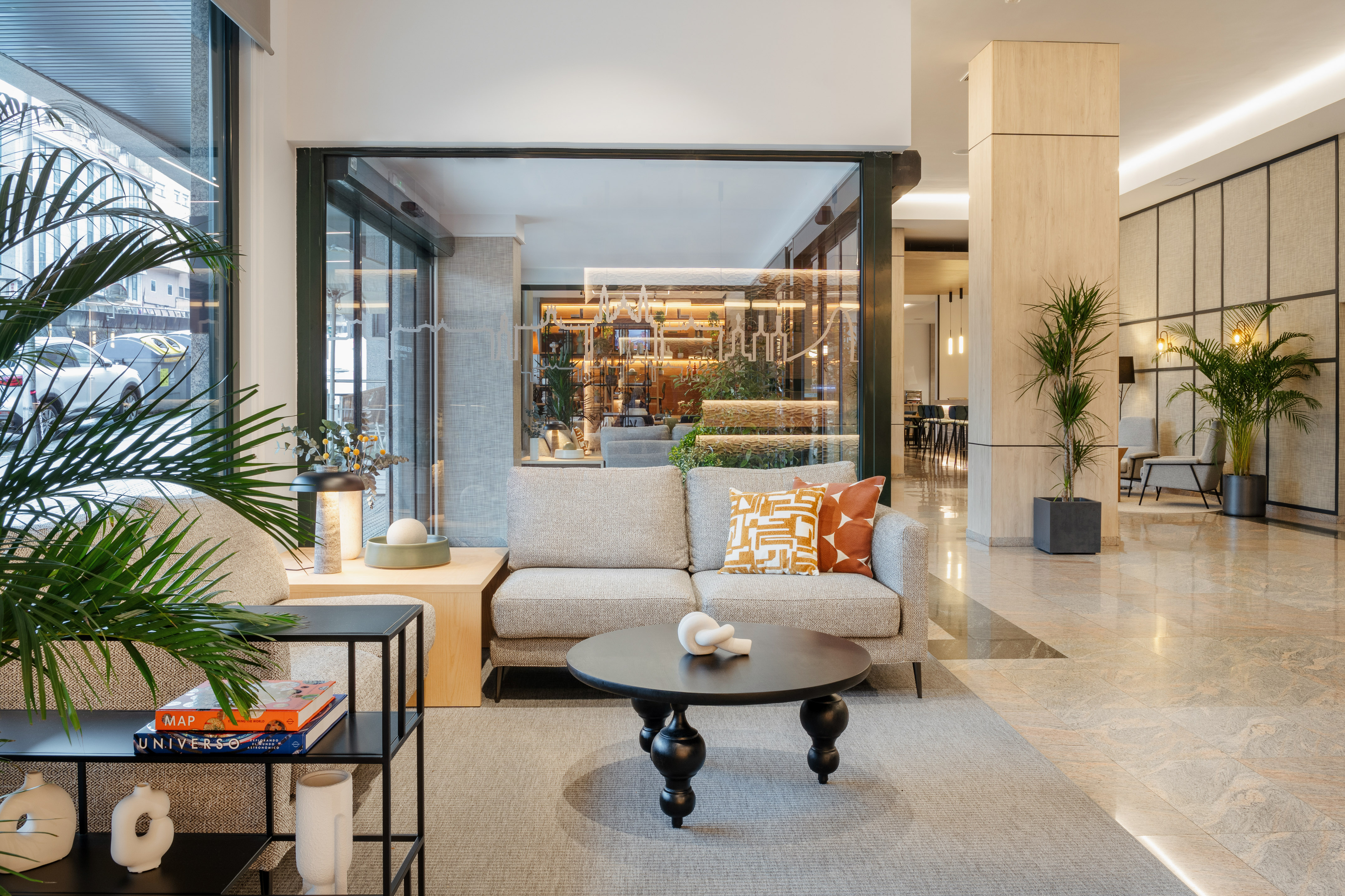 Modern hotel lobby lounge with sofa, coffee table, and lush green plants.
