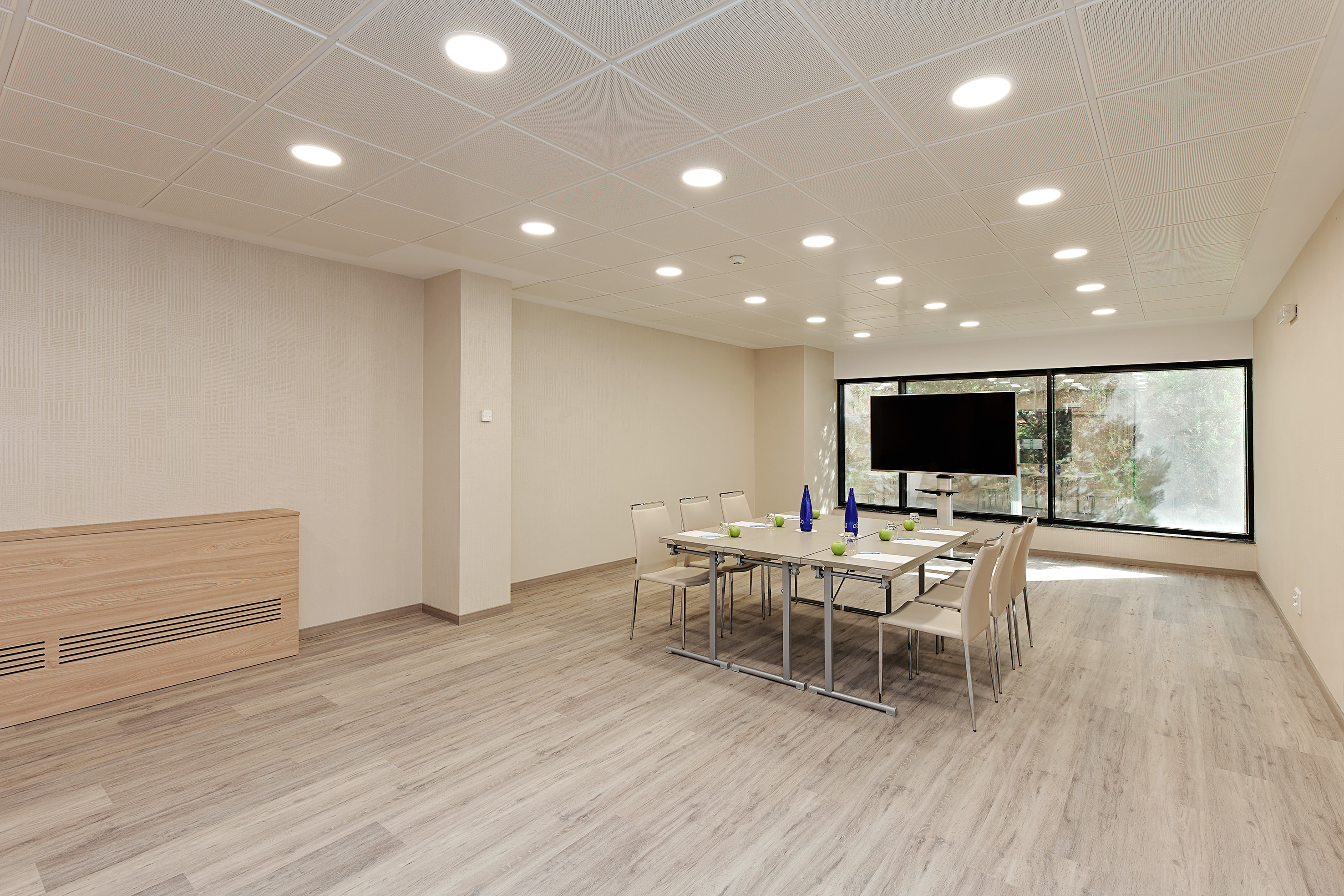 Bright, modern meeting room with large screen, conference table, chairs, and window.