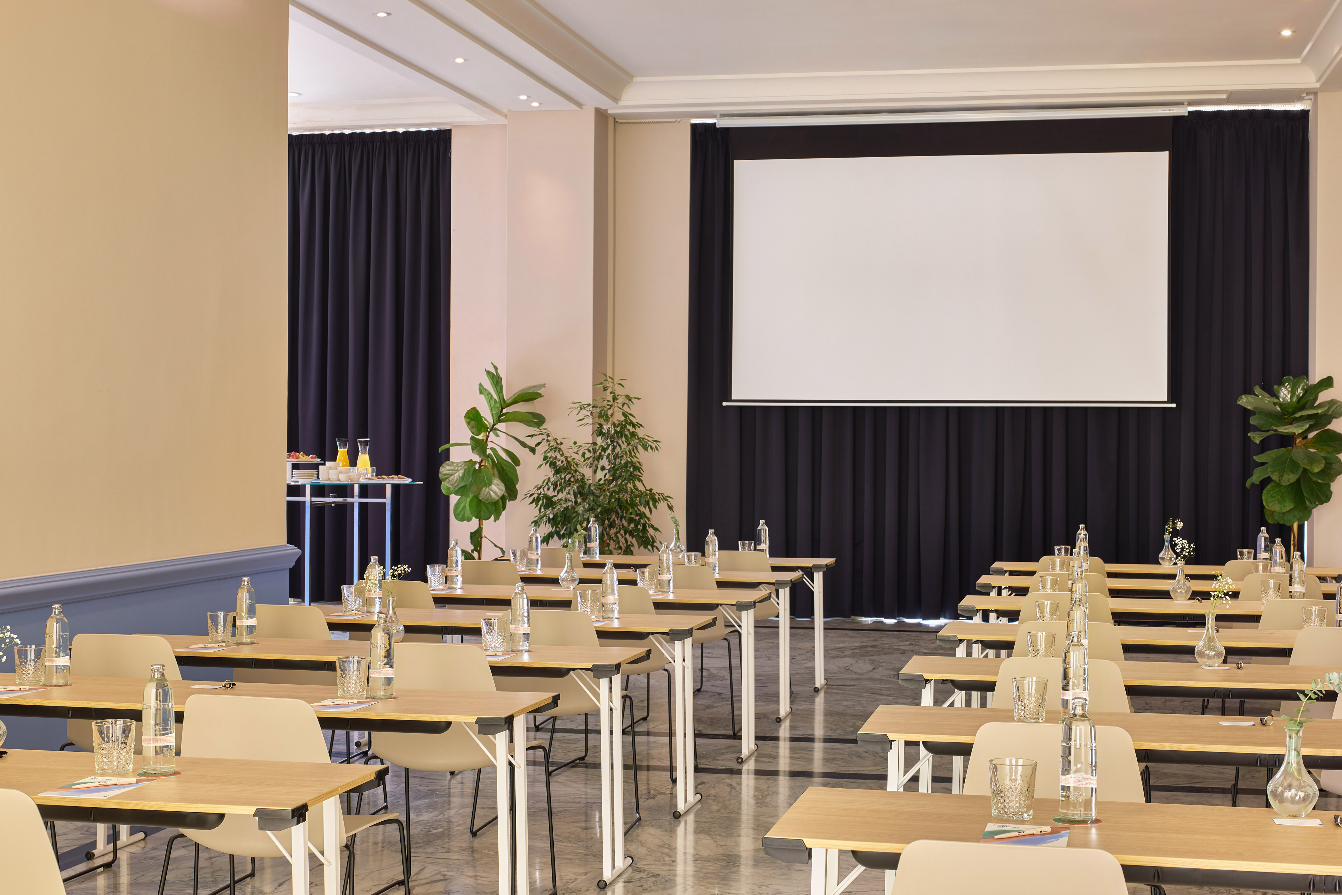 Conference room setup with tables, chairs, water, and projection screen.