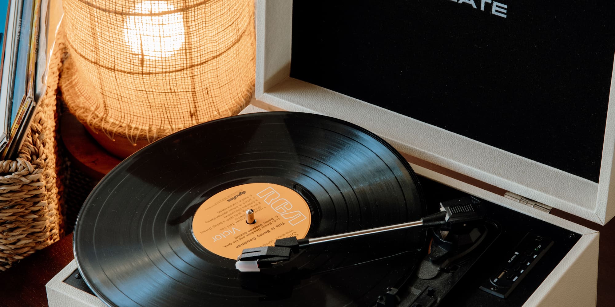 Vintage cream CREATE record player playing vinyl, beside warm burlap lamp.